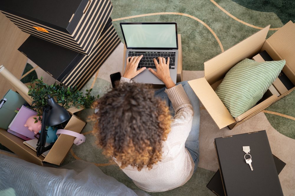 White person typing on laptop amidst packed boxes and household items