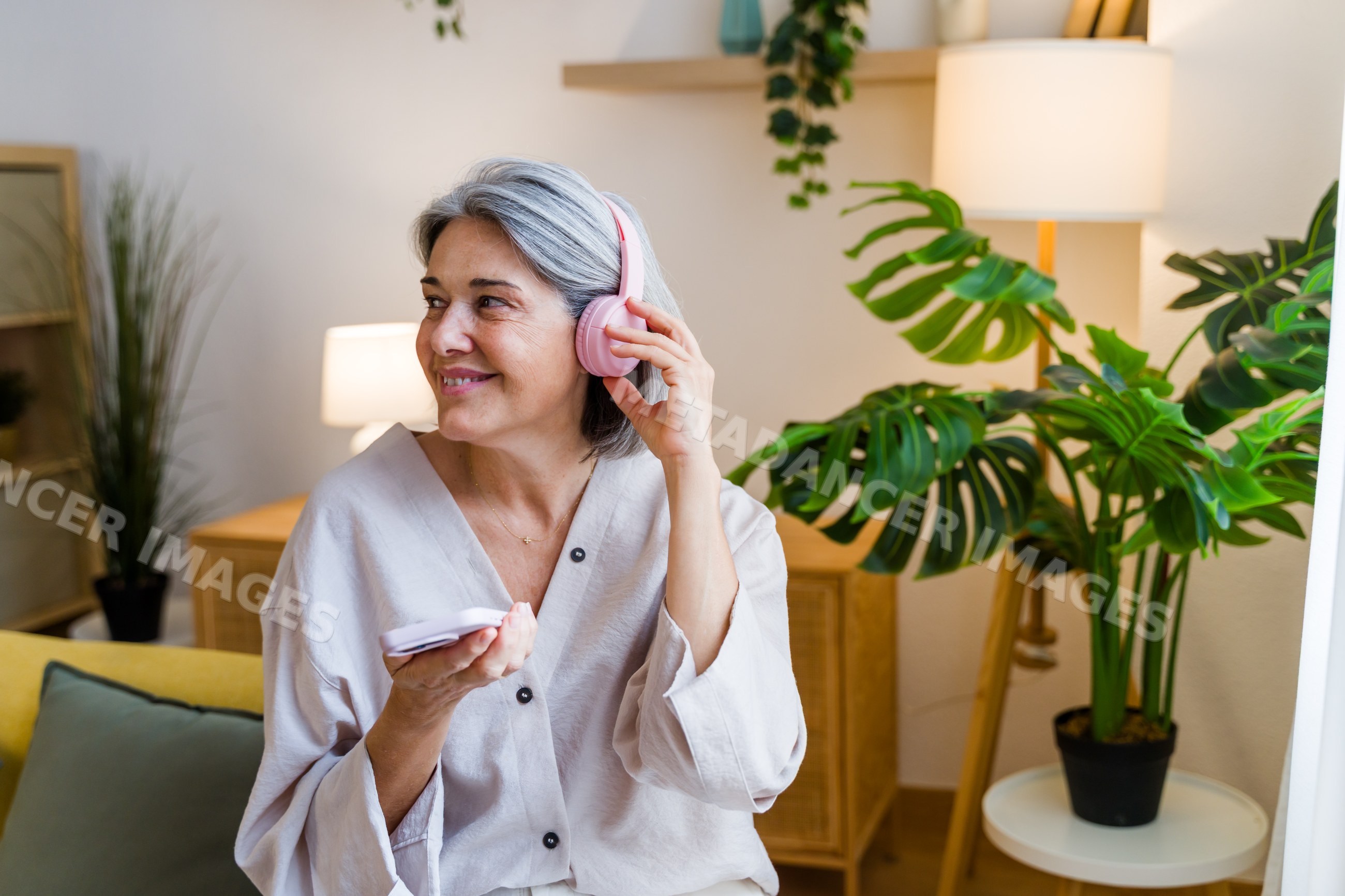 White woman wearing headphones holding tablet in cozy indoor setting