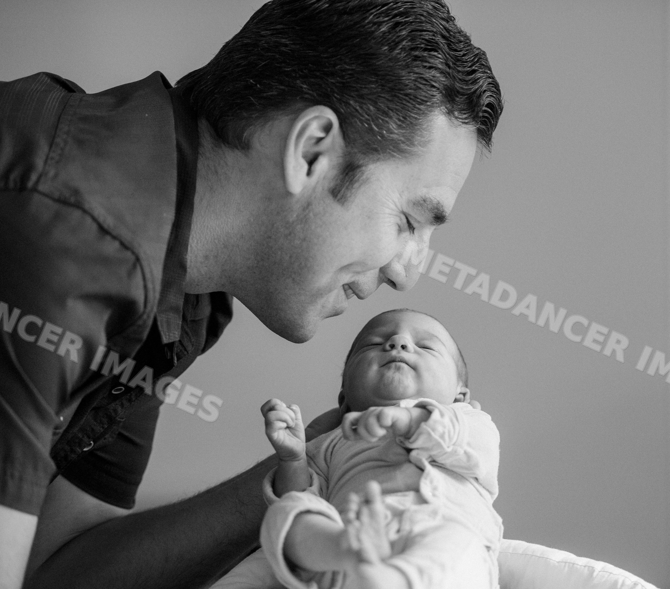 Father lovingly smiles at his newborn baby indoors