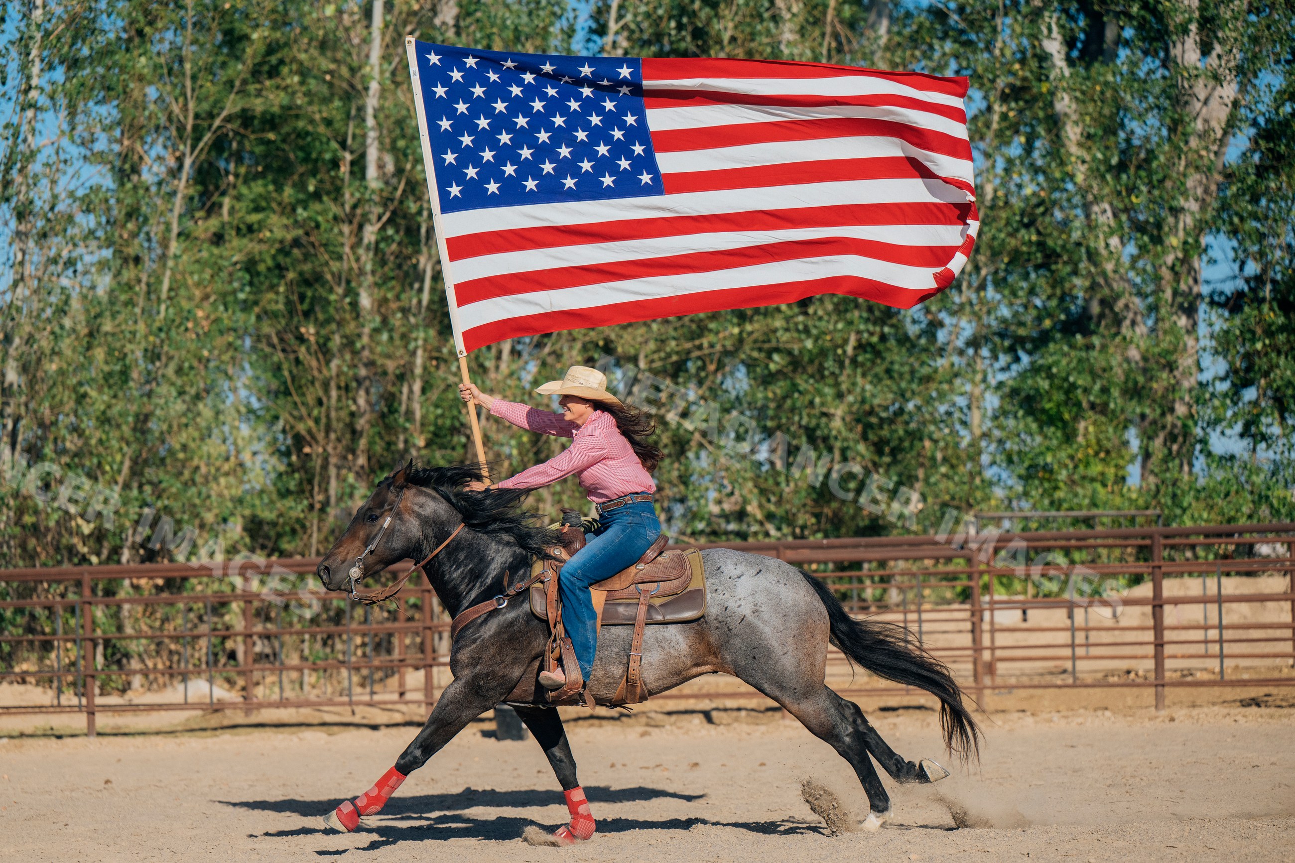 White woman riding horse holding american flag in rodeo arena