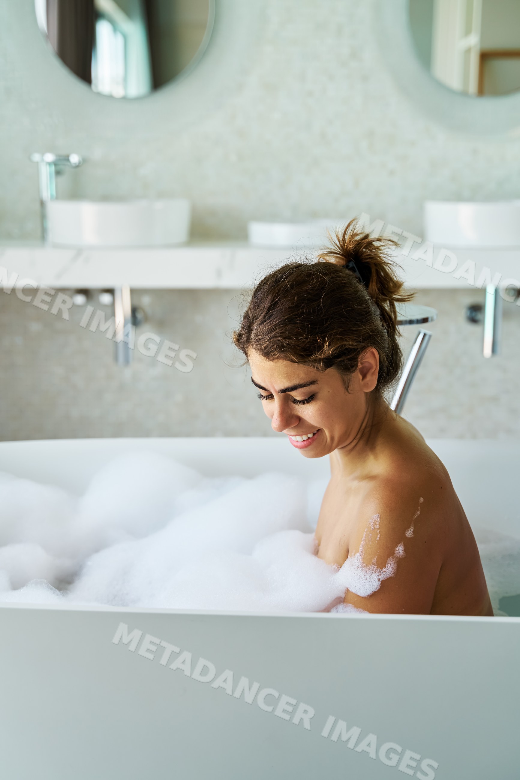 A white woman smiling and relaxing in a bathtub with bubbles