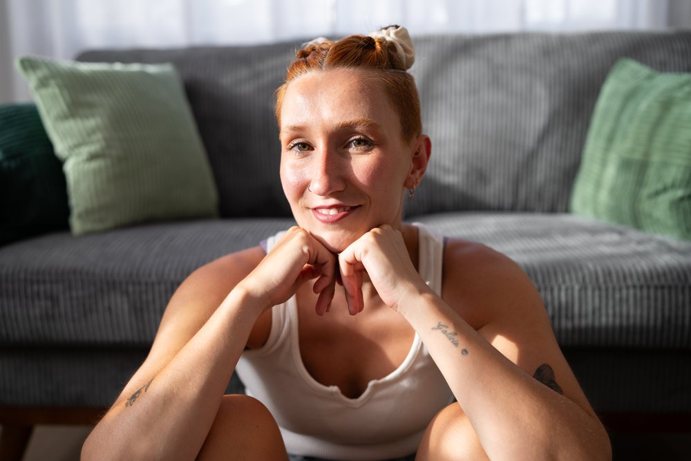 A white woman with tattoos smiling while sitting in her living room