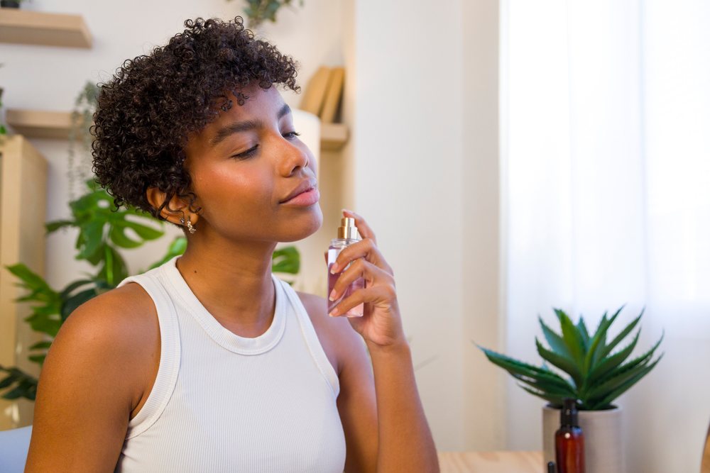African American woman spraying fragrance indoors near potted plant