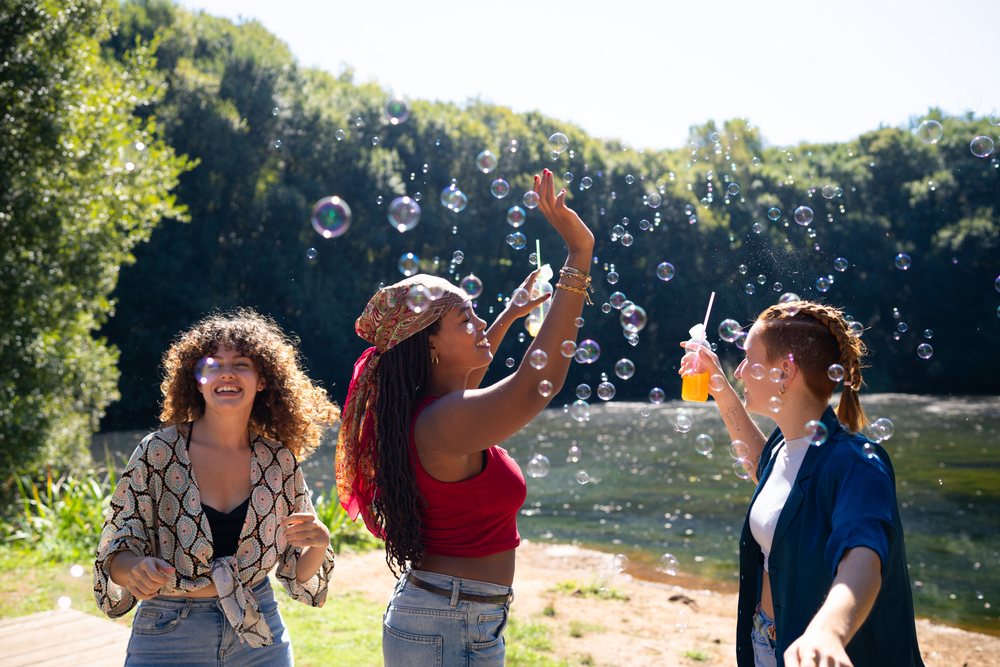 White and African American women enjoying bubbles and drinks by lake