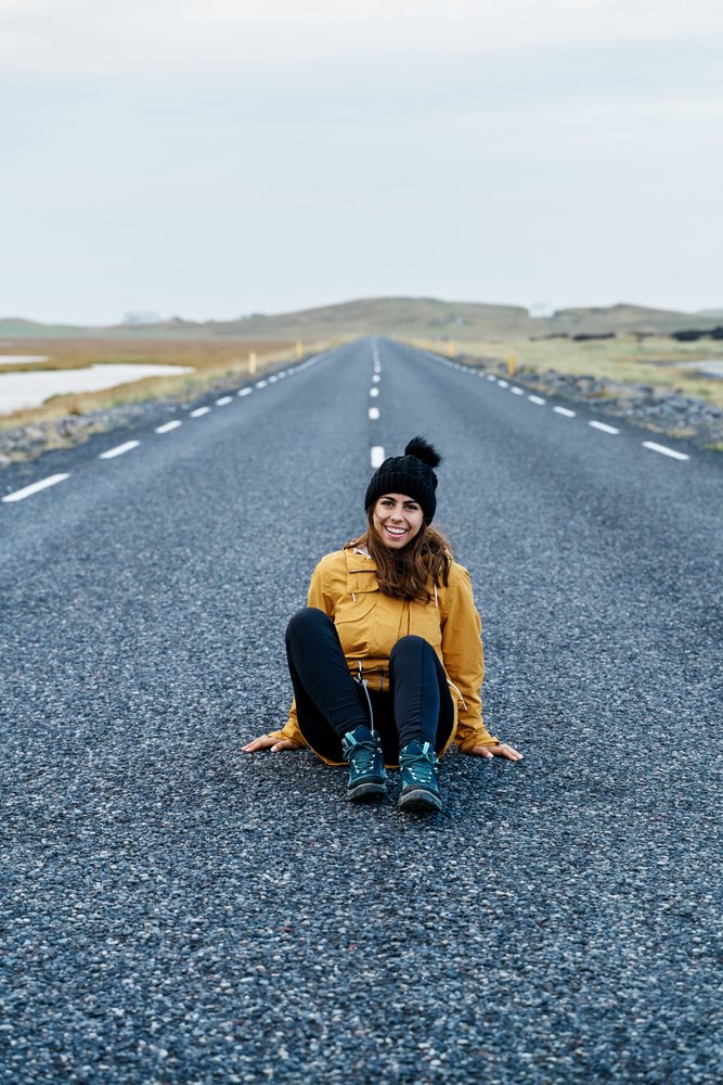 A white woman in a yellow jacket sitting on an empty road