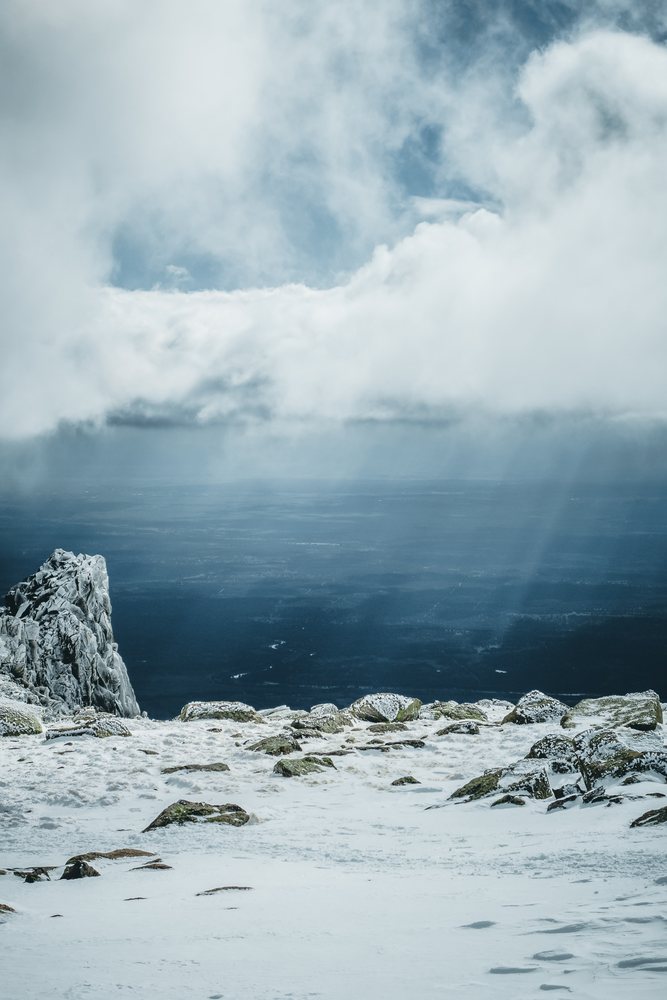 Snow-covered rocky mountaintop with clouds and distant lowlands