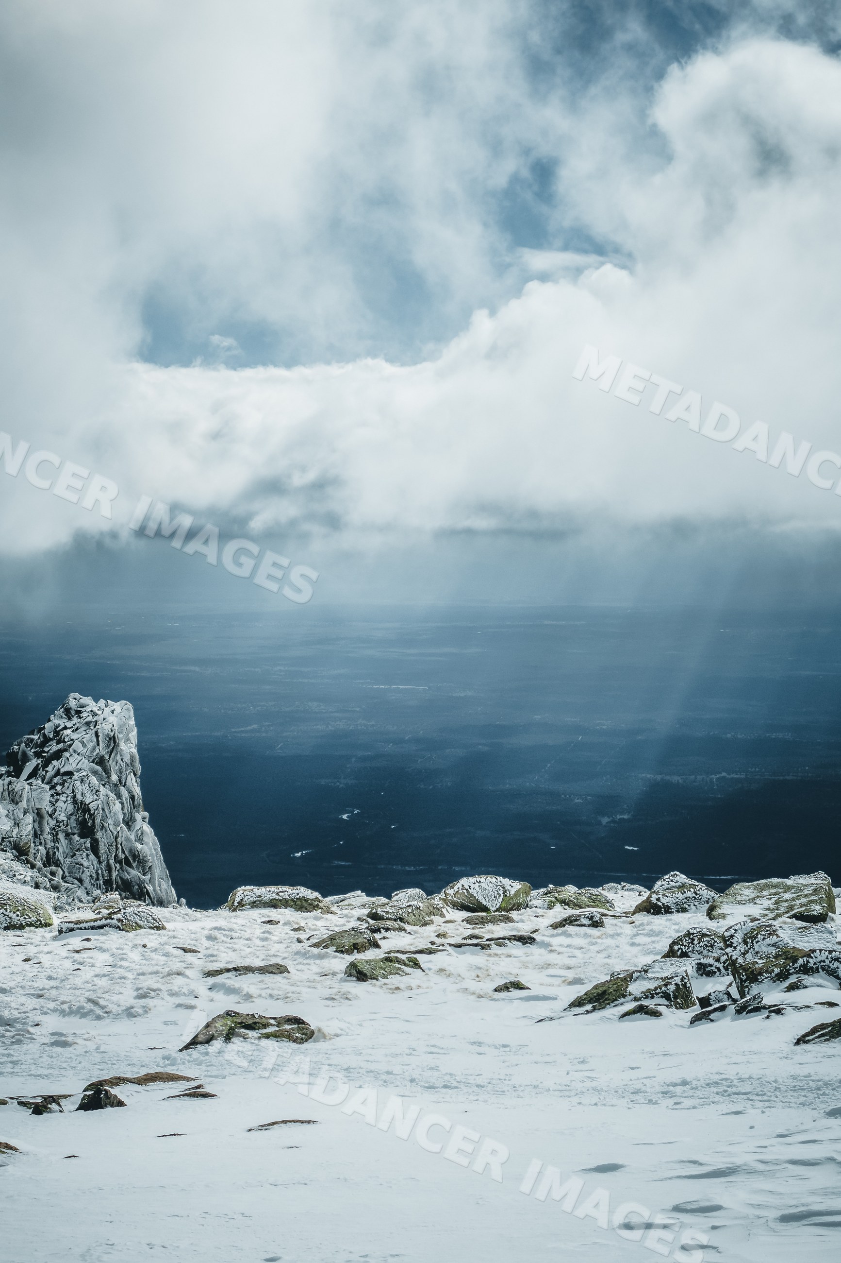 Snow-covered rocky mountaintop with clouds and distant lowlands