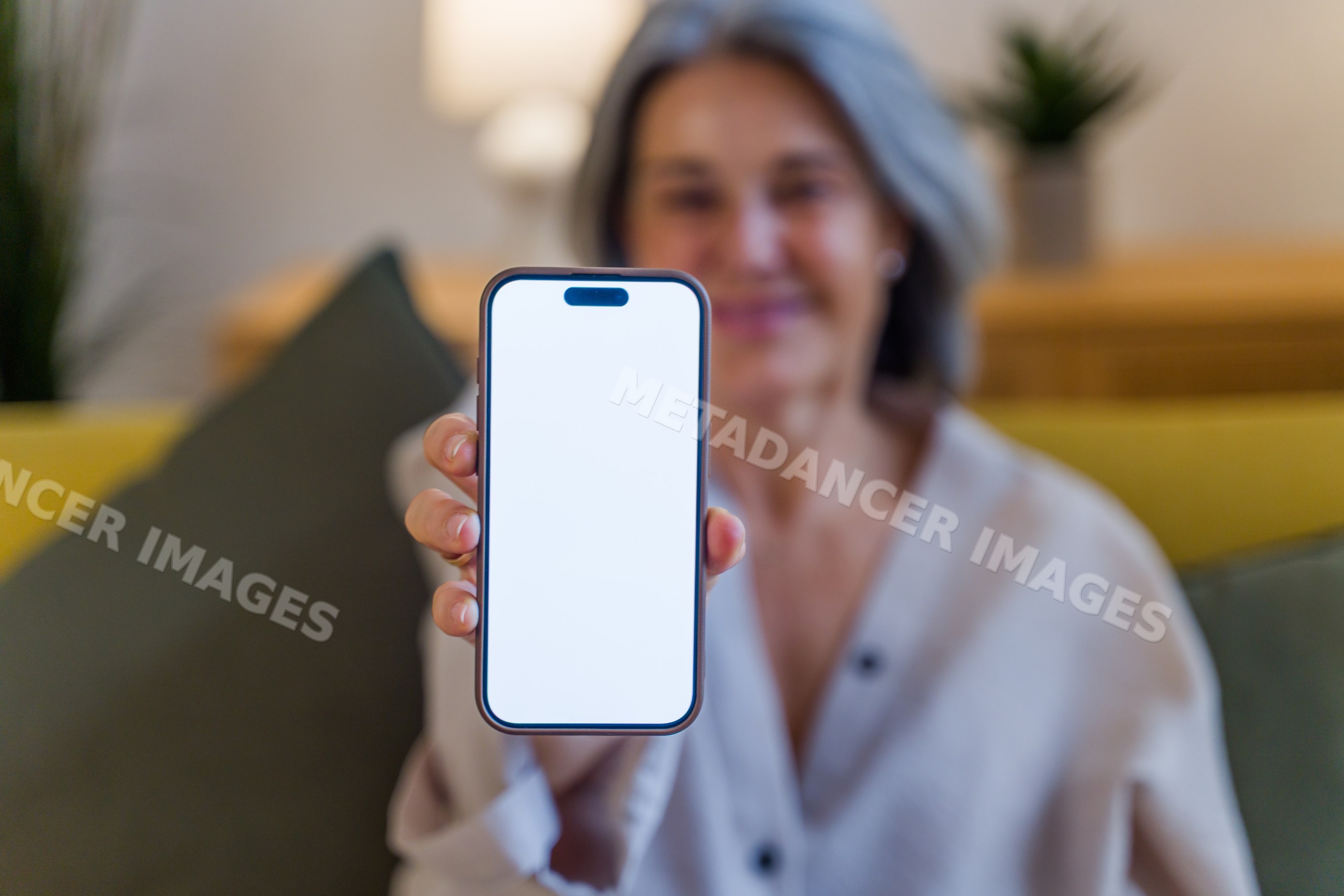 Senior white woman showing smartphone with blank screen indoors