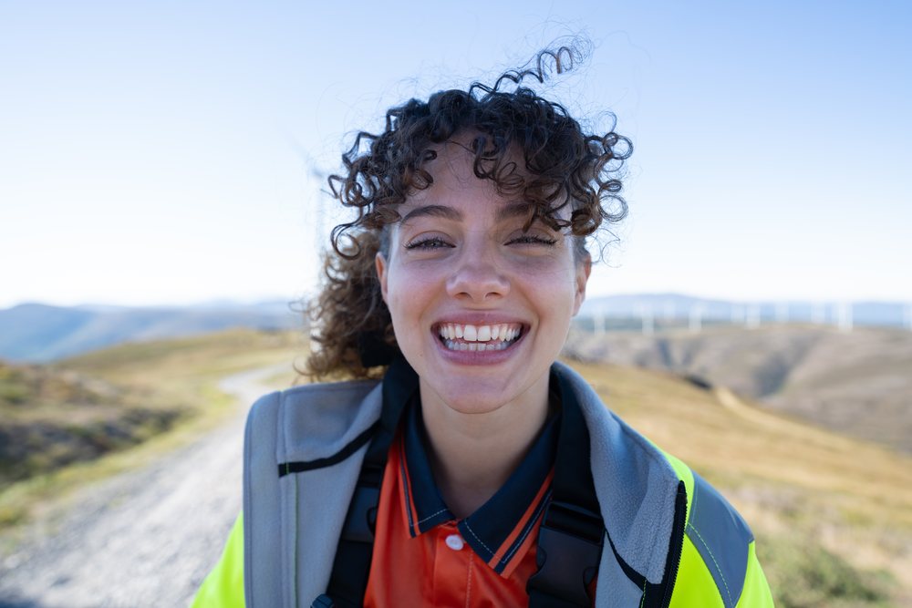 White woman smiling outdoors with wind turbines