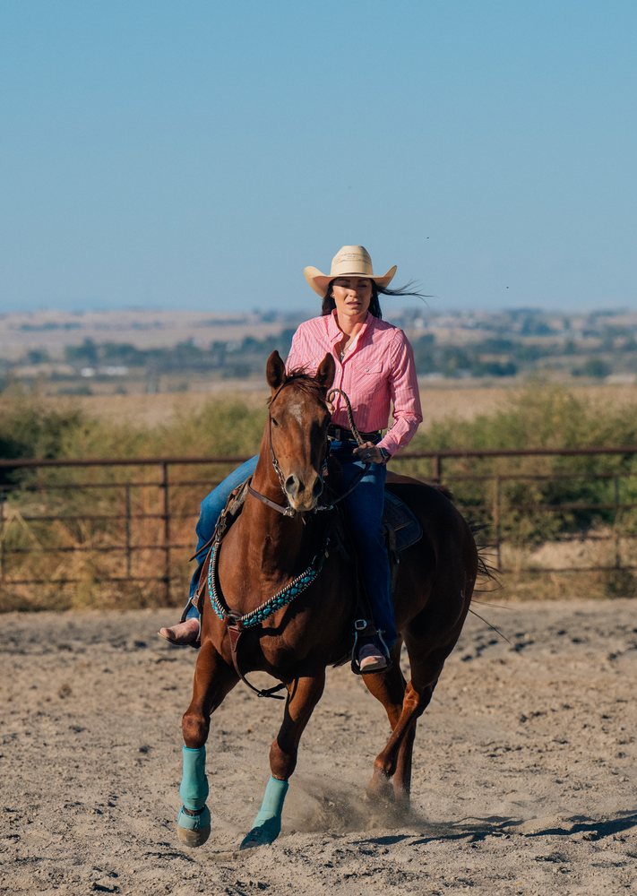 White woman riding horse in open ranch setting