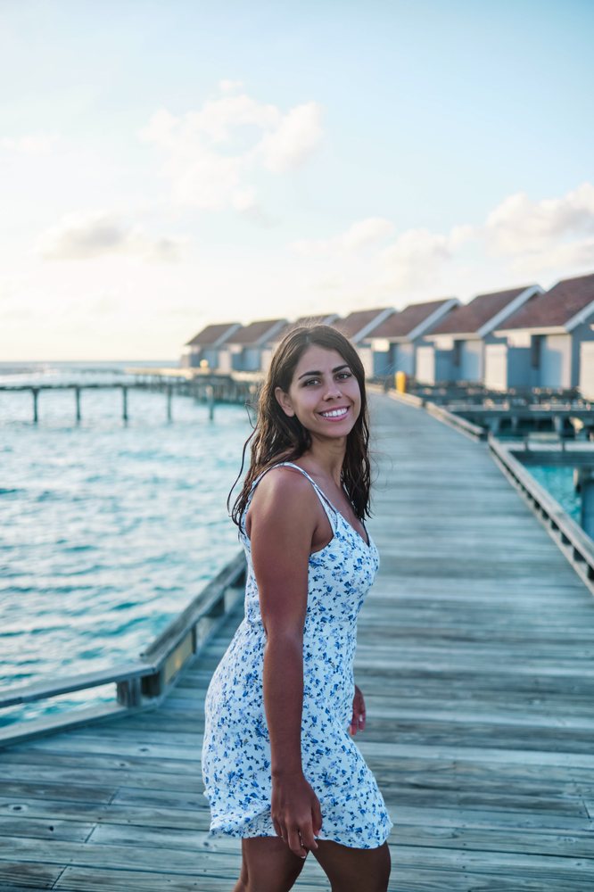 A white woman walks happily on a wooden pier by overwater bungalows