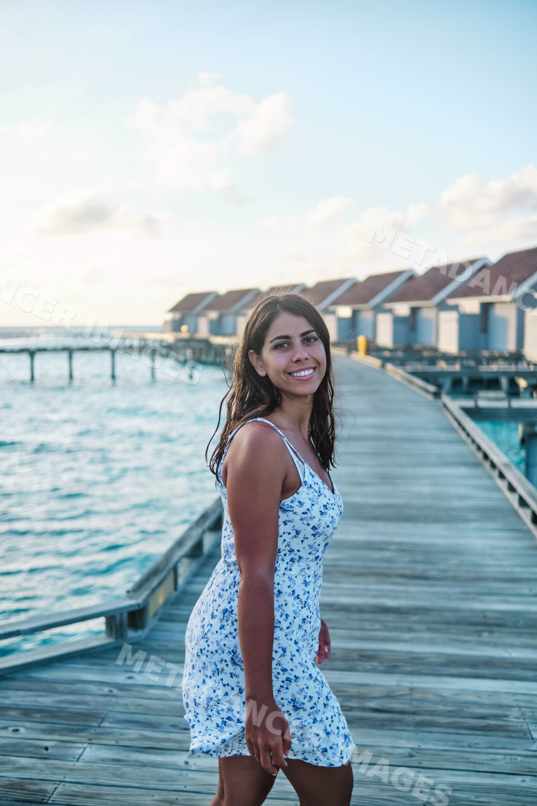 A white woman walks happily on a wooden pier by overwater bungalows