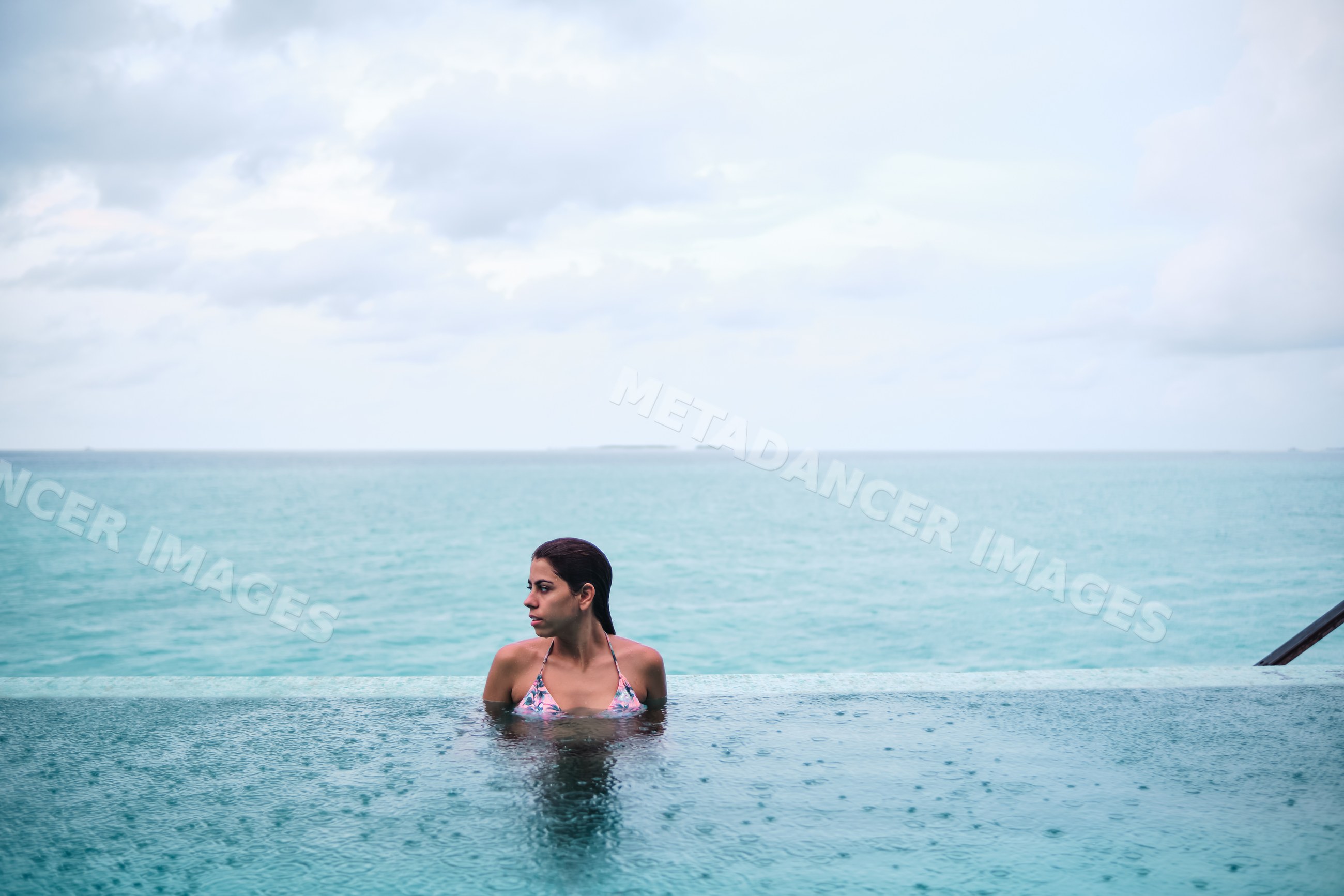 A white woman relaxing in an infinity pool overlooking the ocean