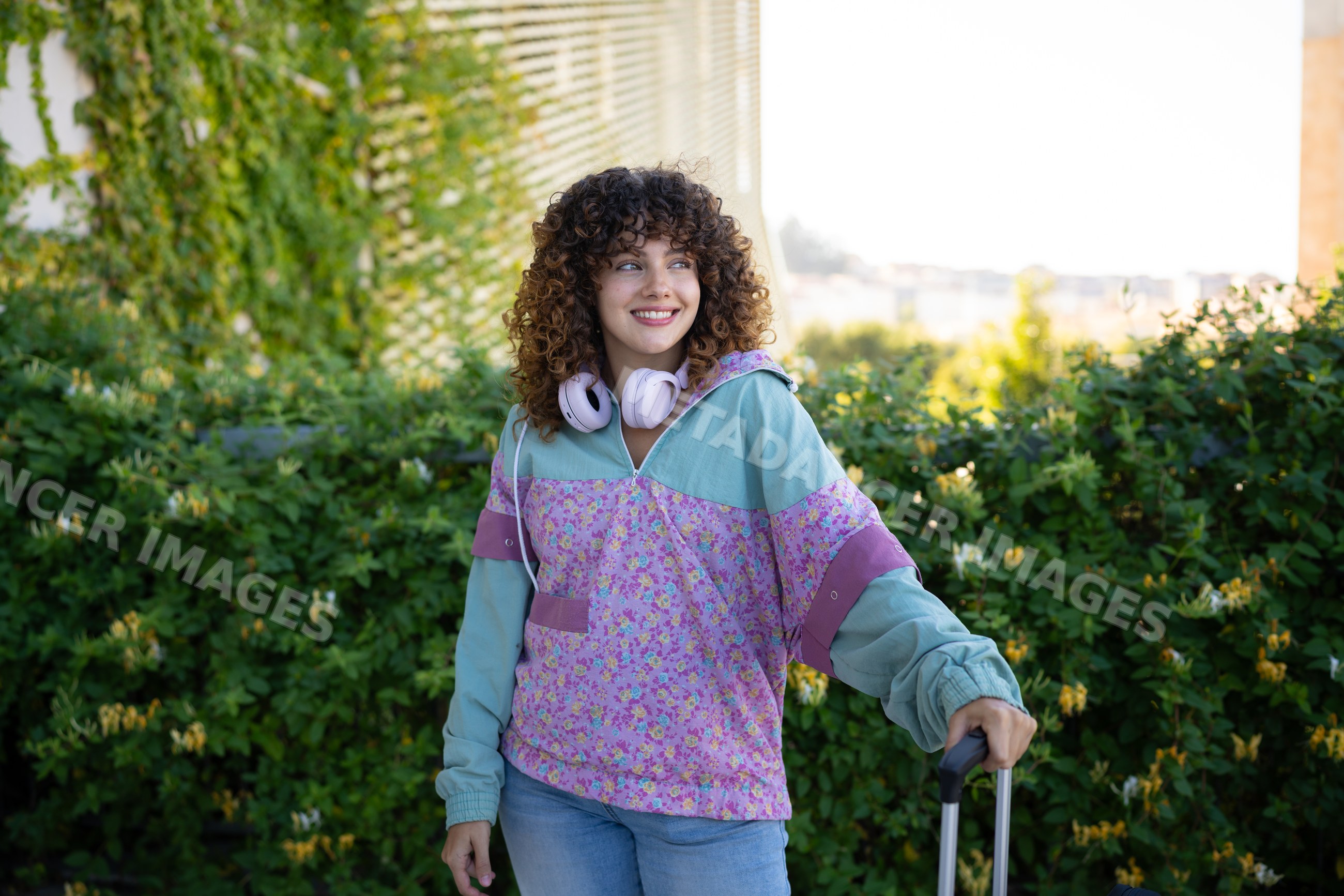 Young white woman with floral hoodie and headphones outdoors holding