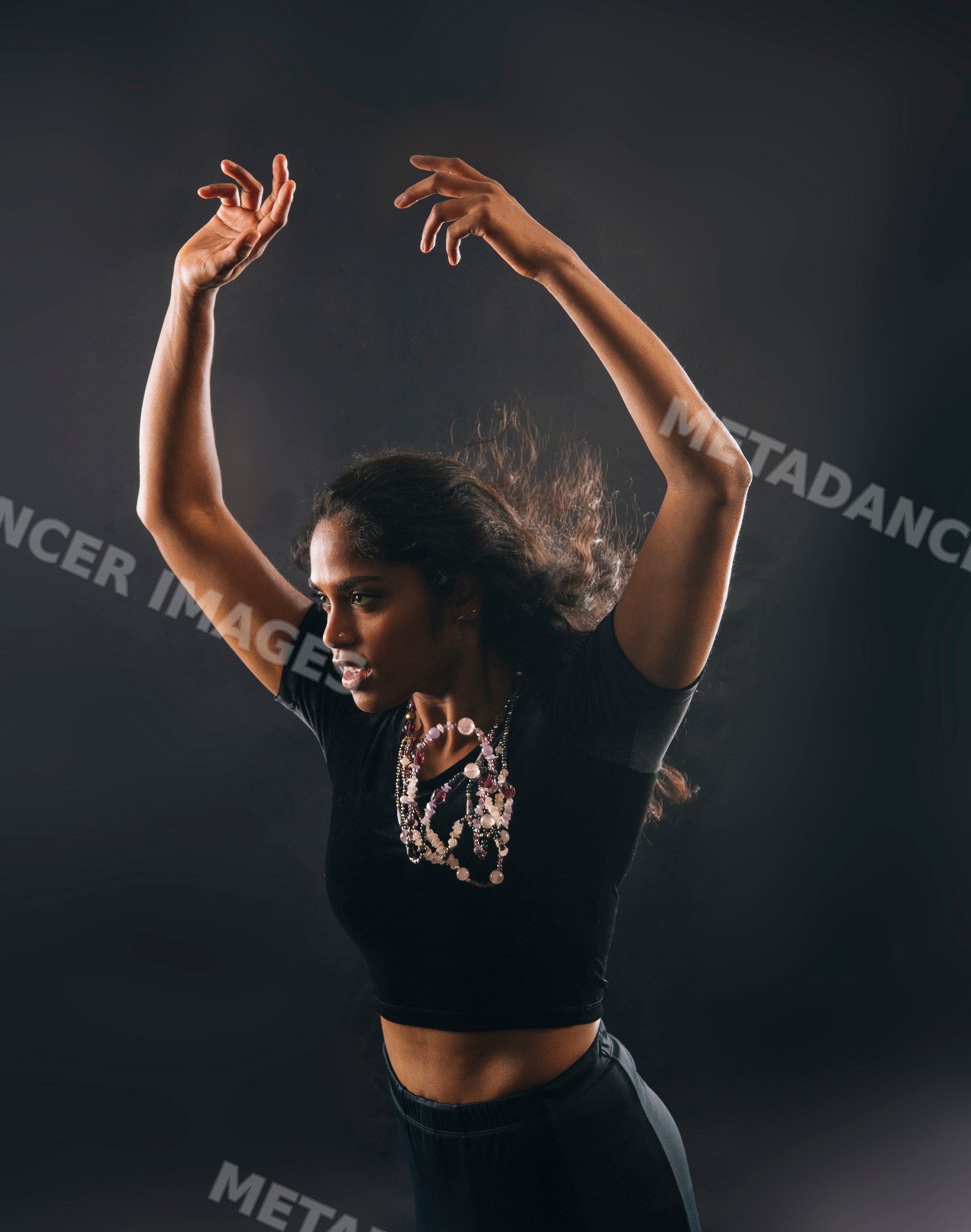 South Asian woman dancing with raised arms and black crop top