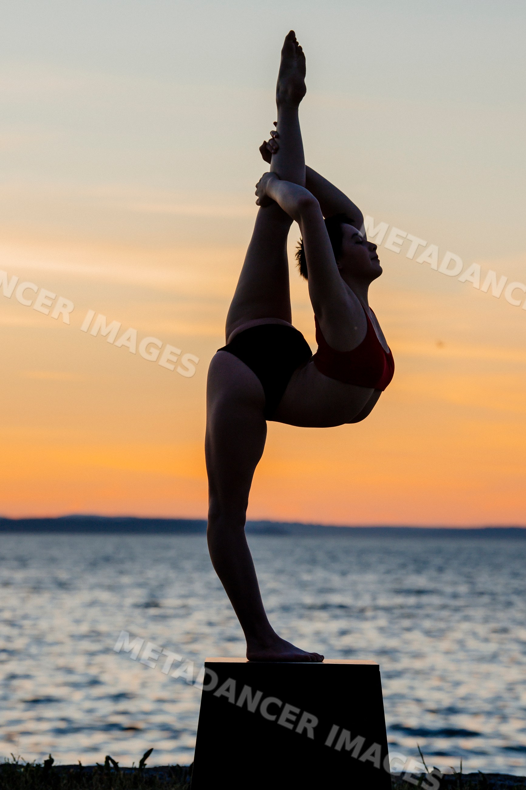 White woman performing yoga stretch pose at sunset by the sea