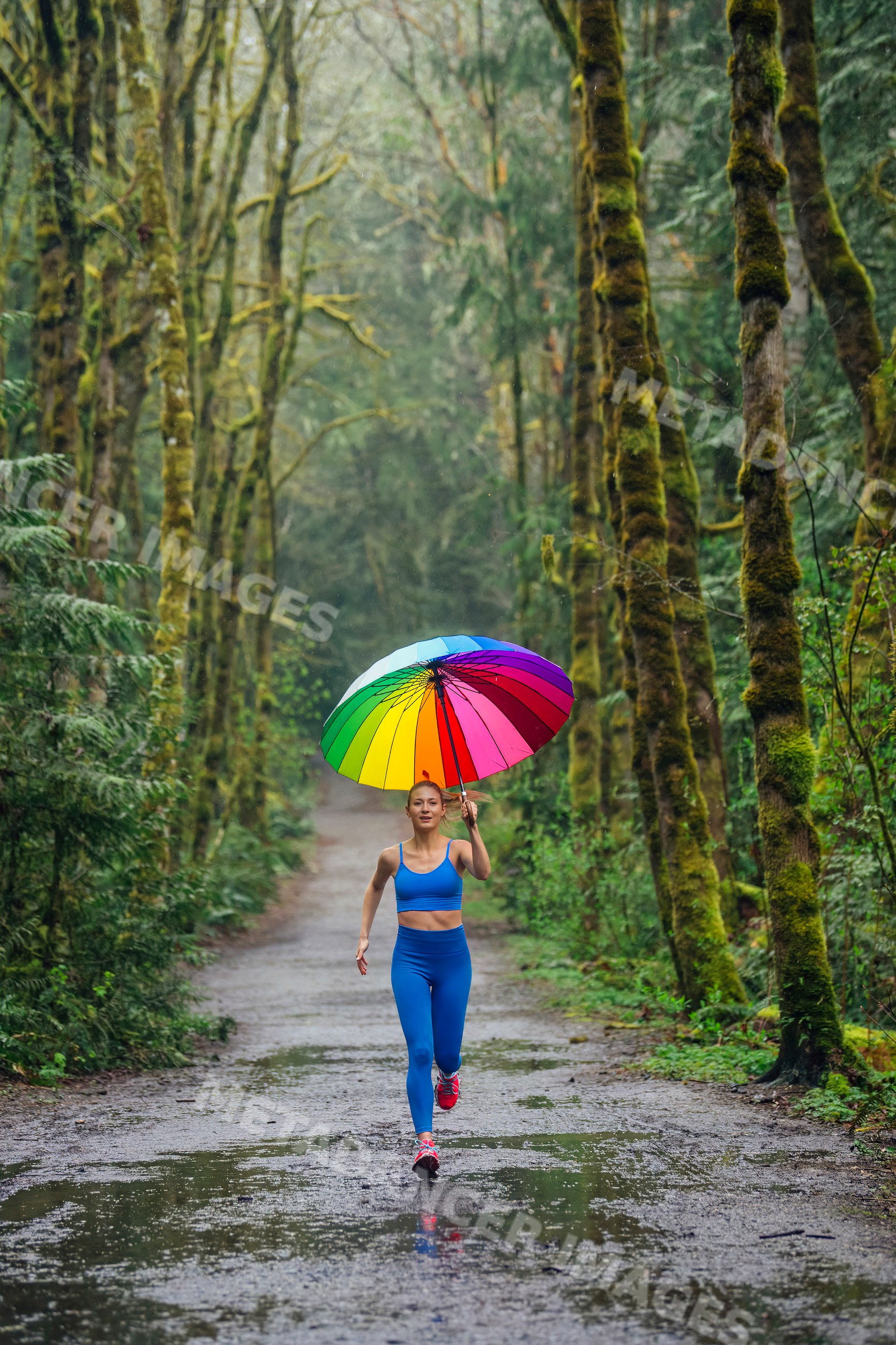 White woman running on rainy forest trail holding rainbow umbrella