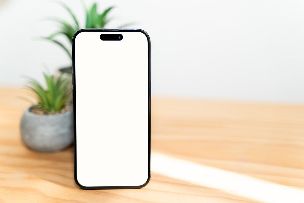 Smartphone with blank screen on wooden table with potted plants