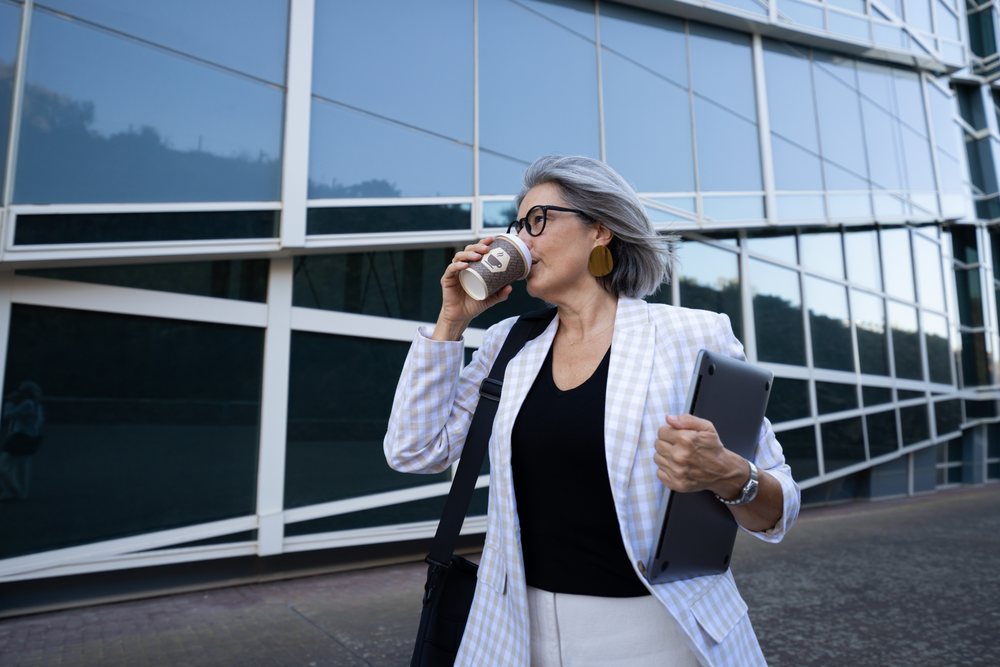 Businesswoman drinking coffee outside office holding laptop