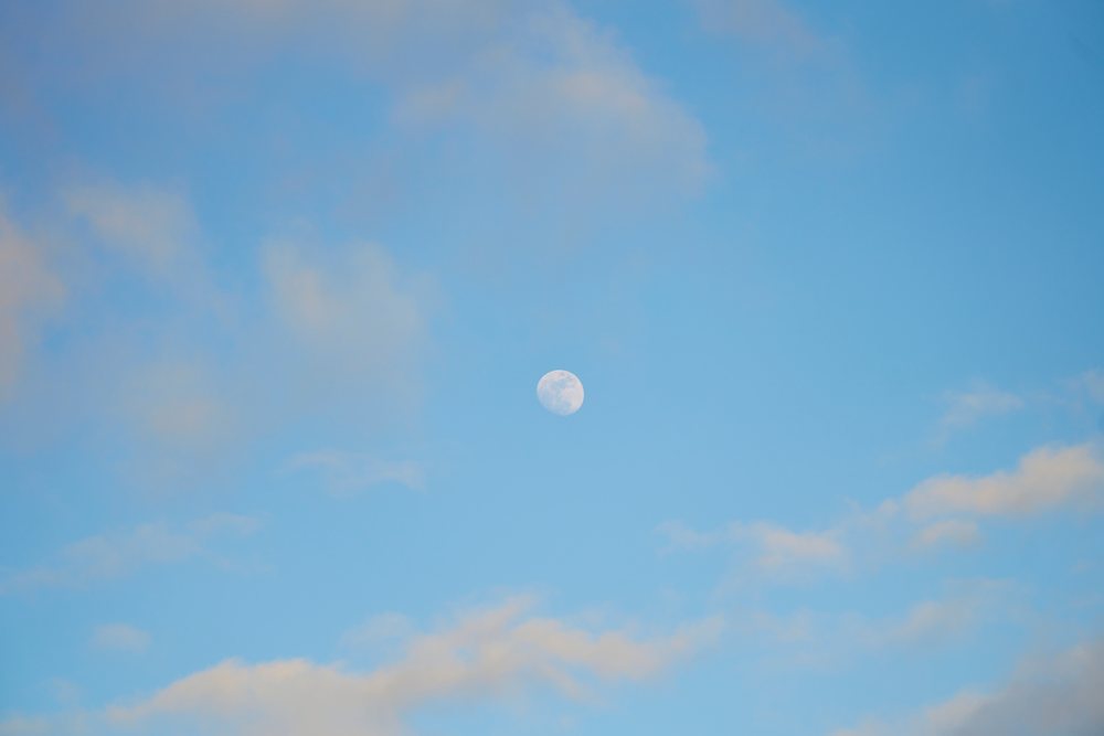 Daytime moon seen in blue sky with clouds over Oahu, Hawaii