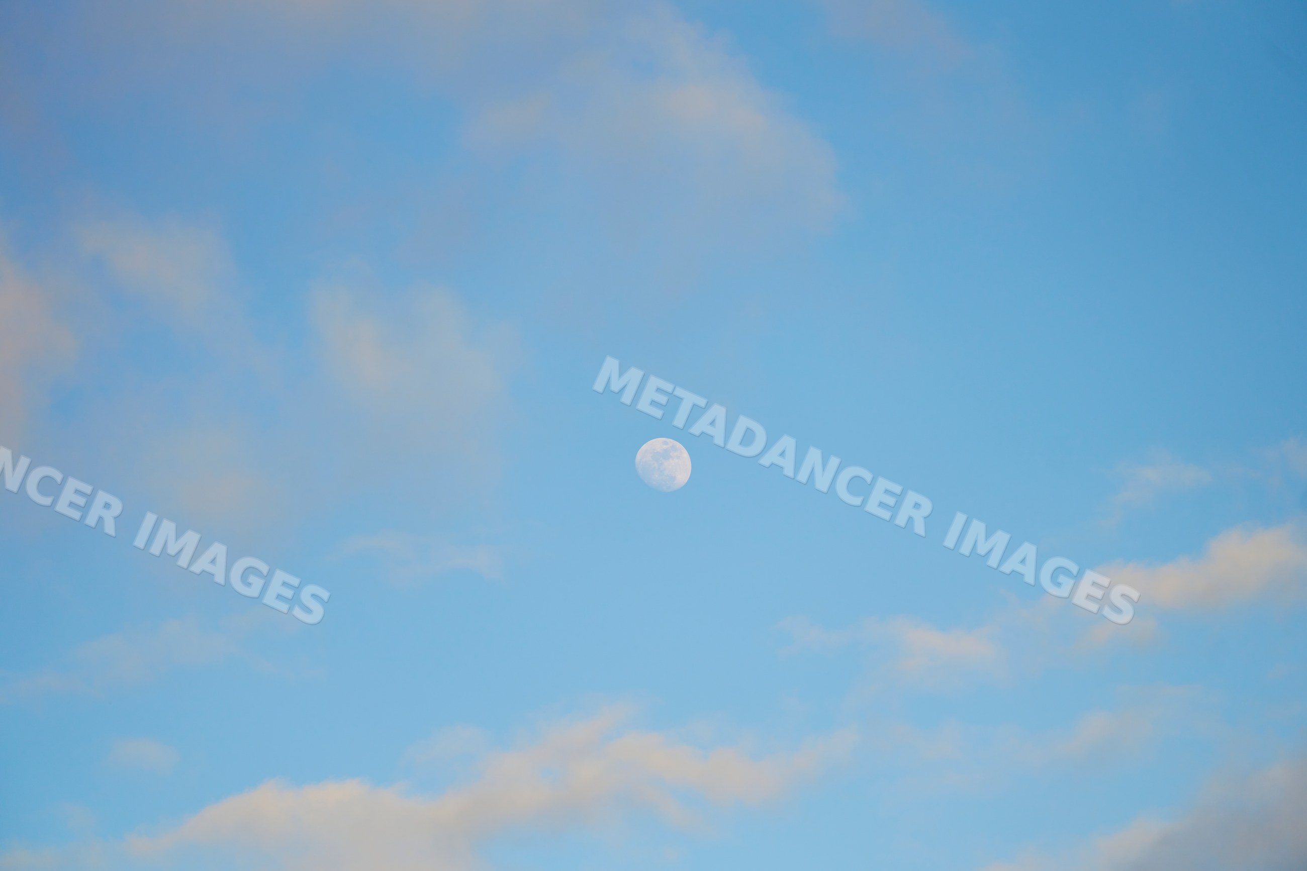 Daytime moon seen in blue sky with clouds over Oahu, Hawaii