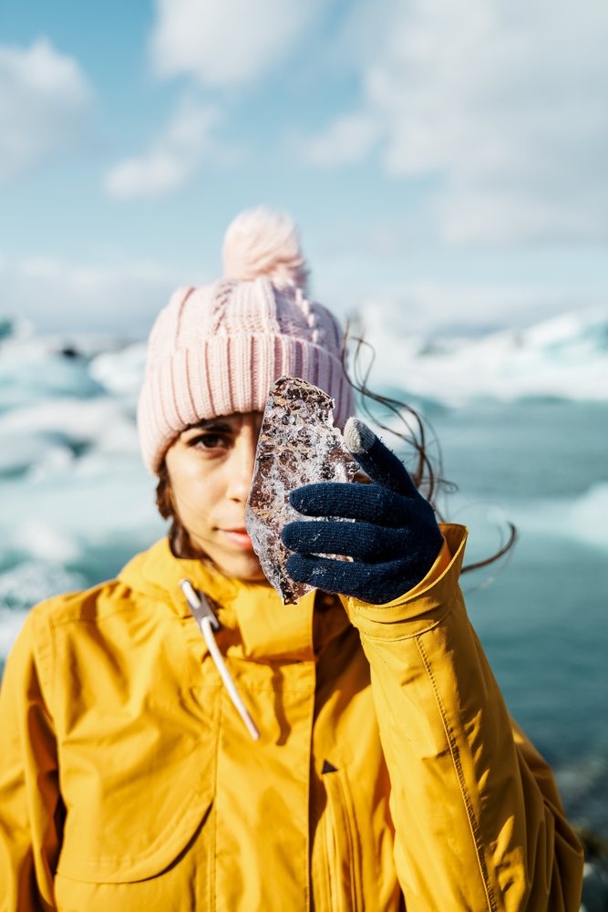 A white woman holds a piece of ice near a frozen landscape