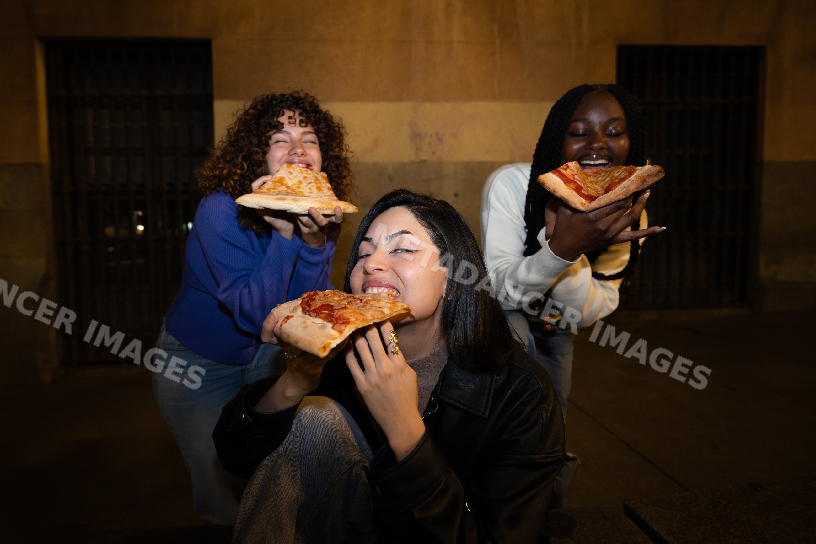 Friends enjoying pepperoni pizza slices outdoors at night