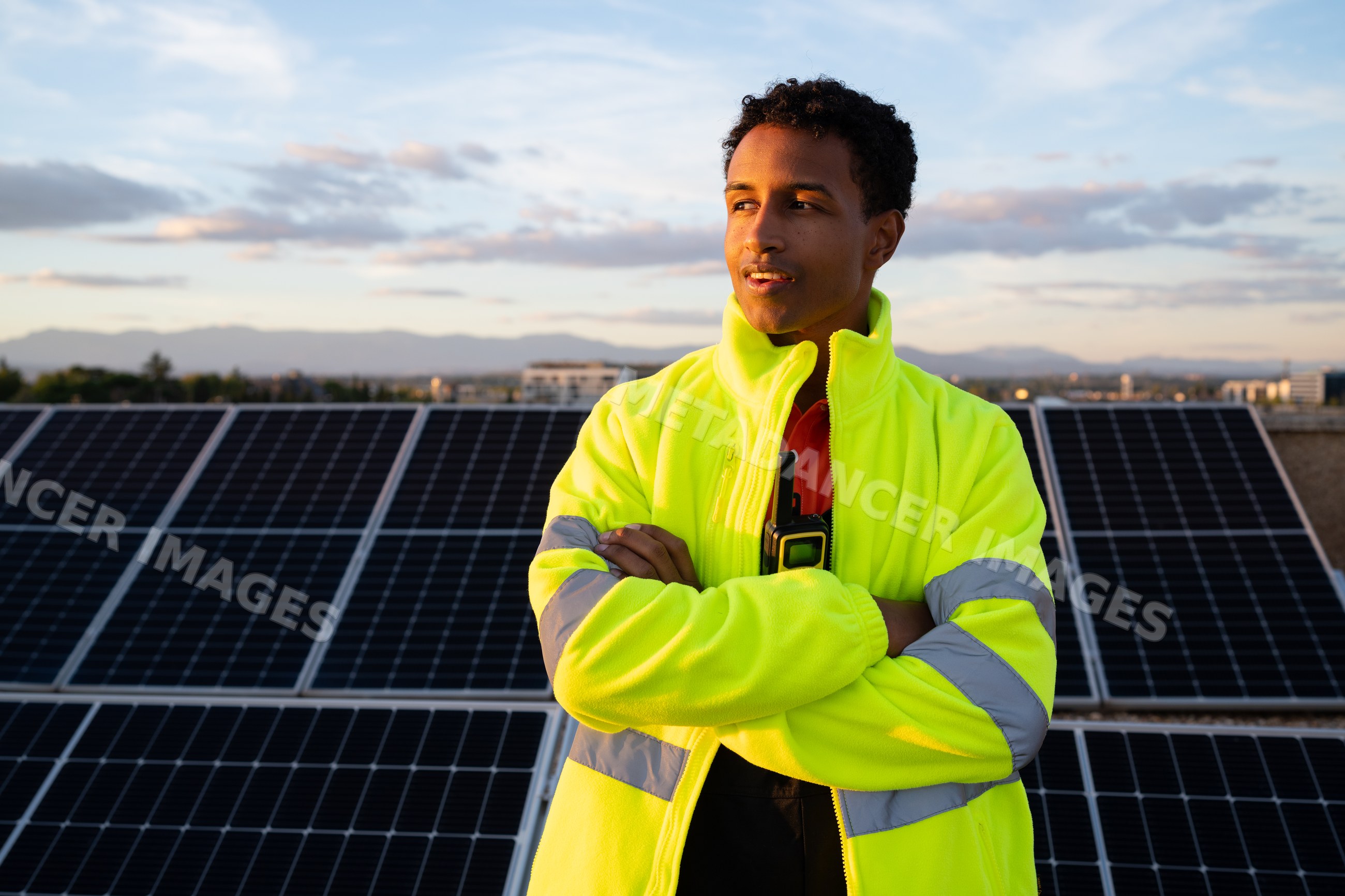 Man in high-visibility jacket standing by solar panels at sunset