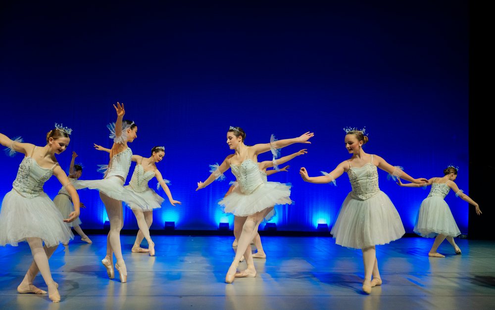 Young ballerinas perform a ballet dance on stage with blue lighting