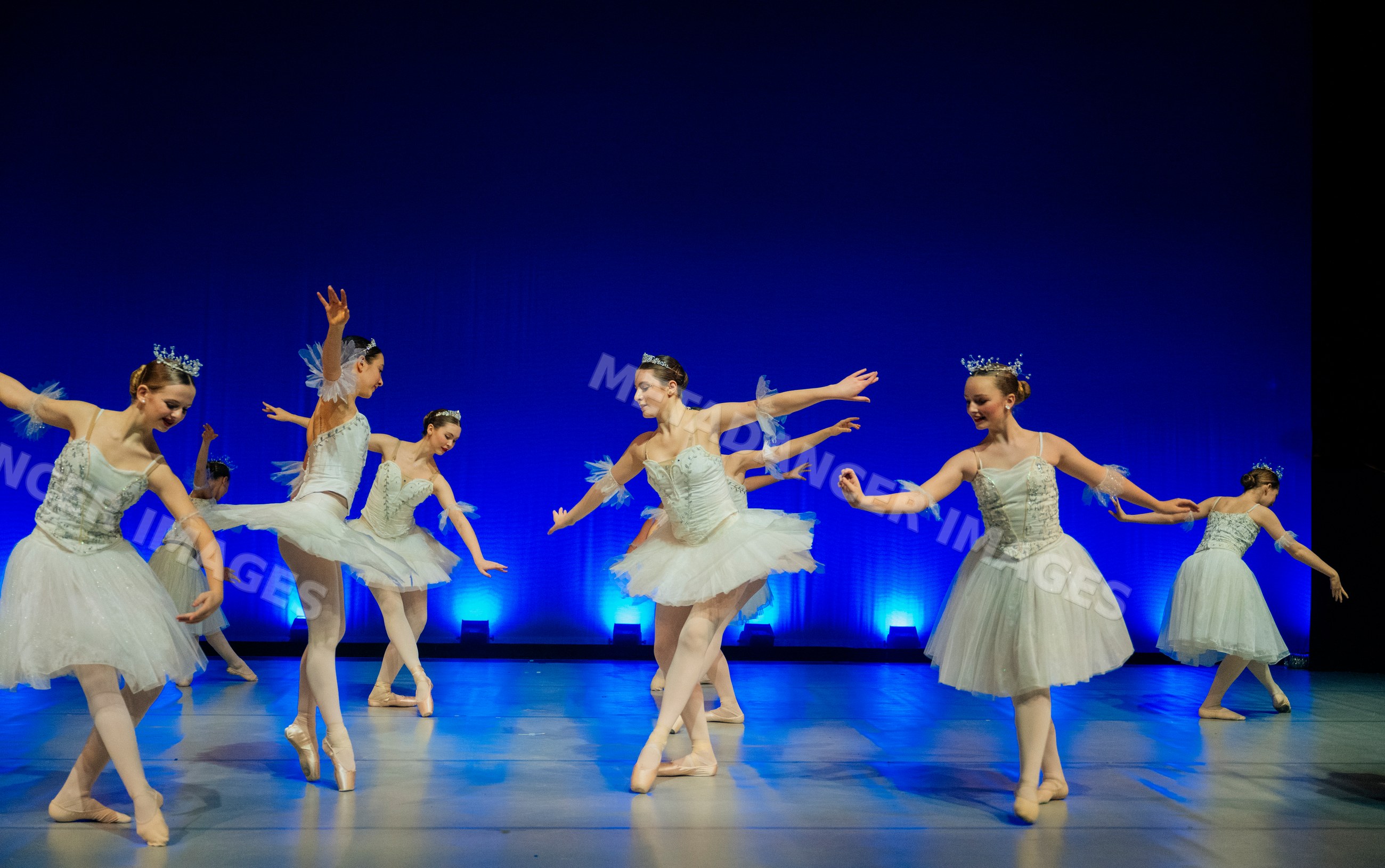 Young ballerinas perform a ballet dance on stage with blue lighting