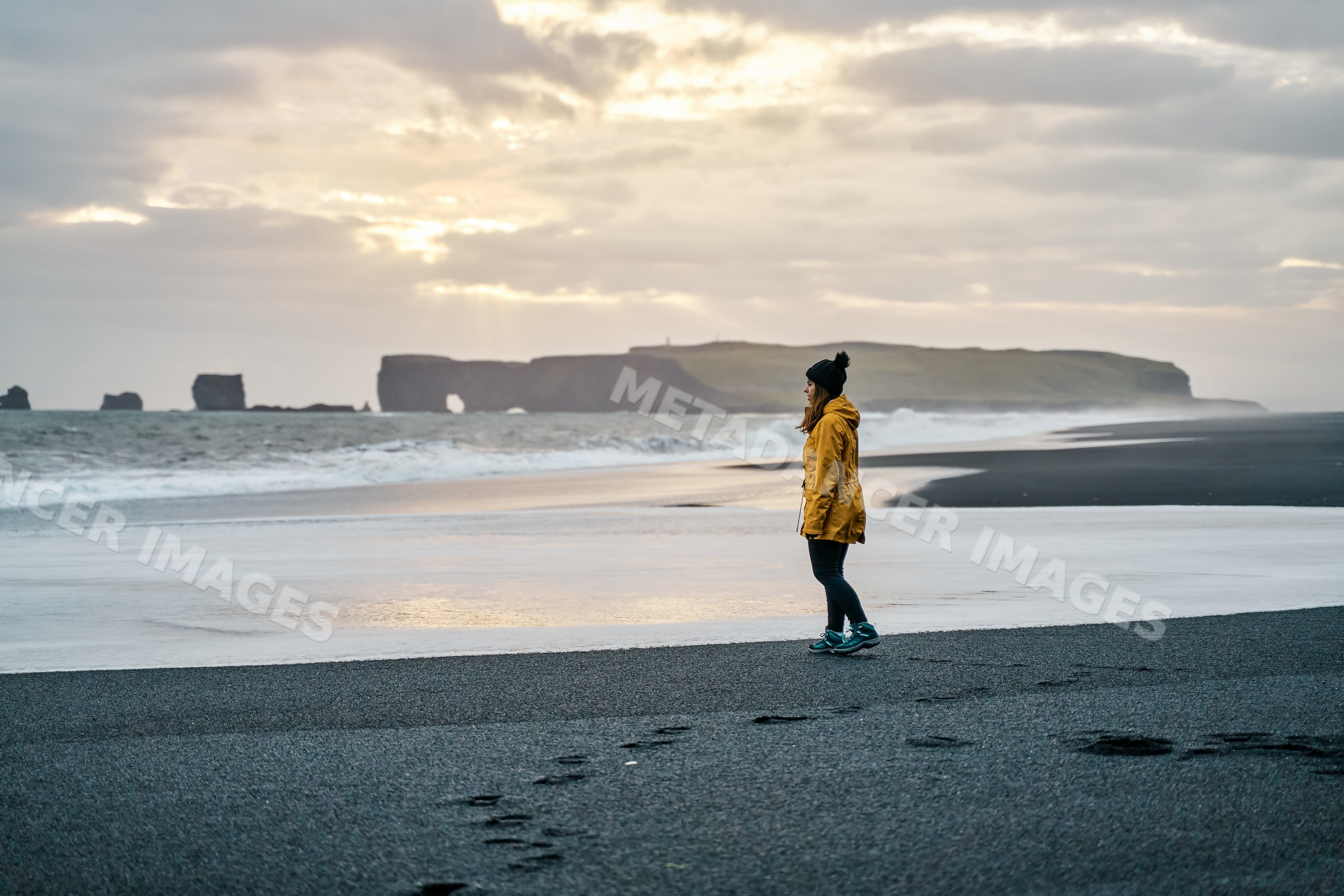 A white woman stands on the black sand beach looking