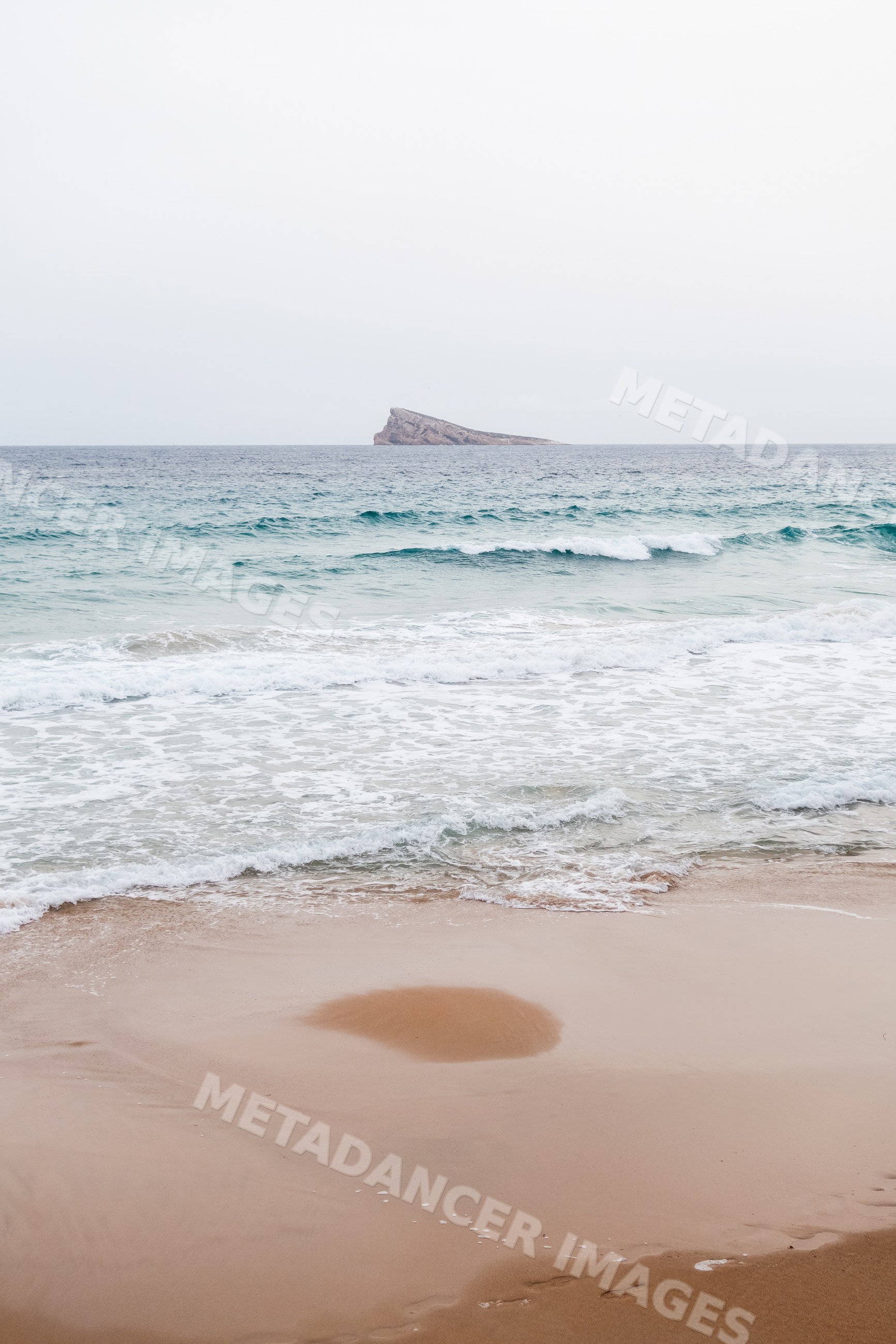 Ocean waves on a sandy beach with distant rocky island in a beach