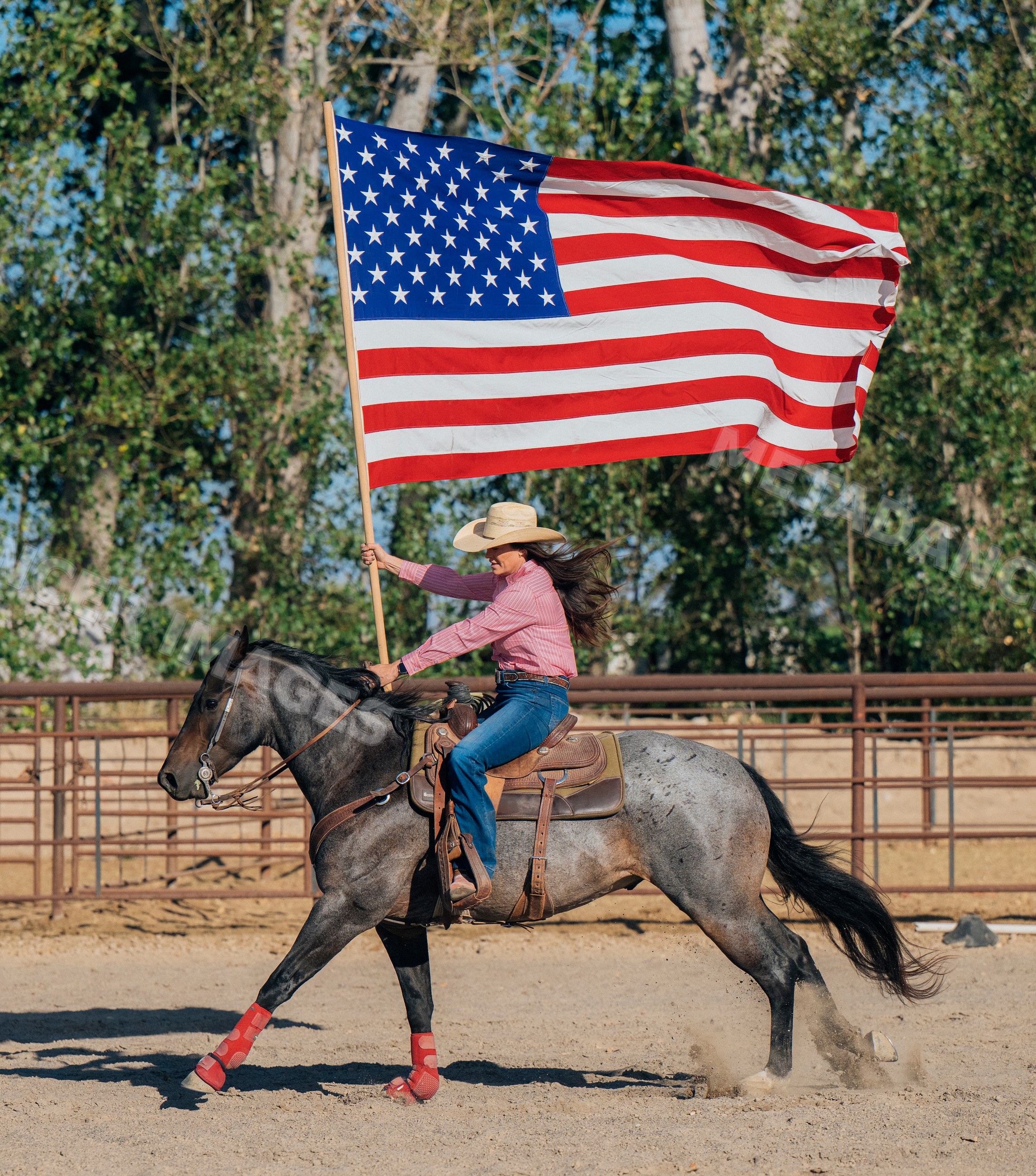 Cowgirl riding horse holding american flag in rodeo arena