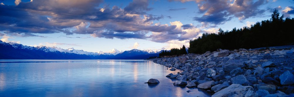 Lake with rocky shoreline and snow-capped mountains under twilight