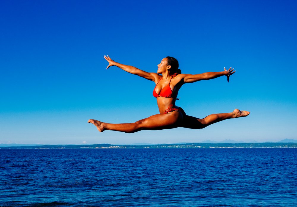 A woman in a red bikini jumps in a split over the ocean in WA, USA