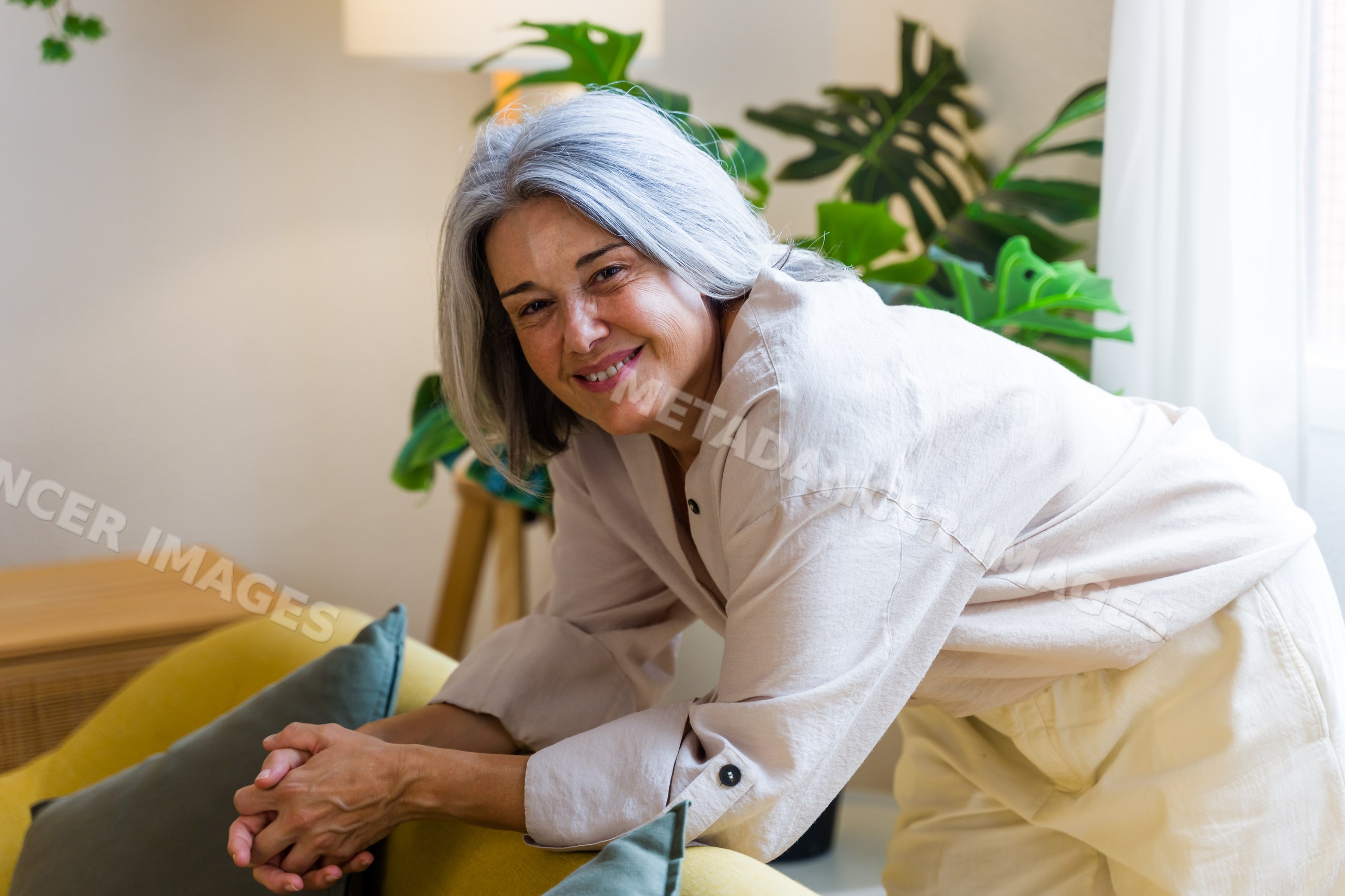 White woman leaning on yellow armchair smiling in home interior
