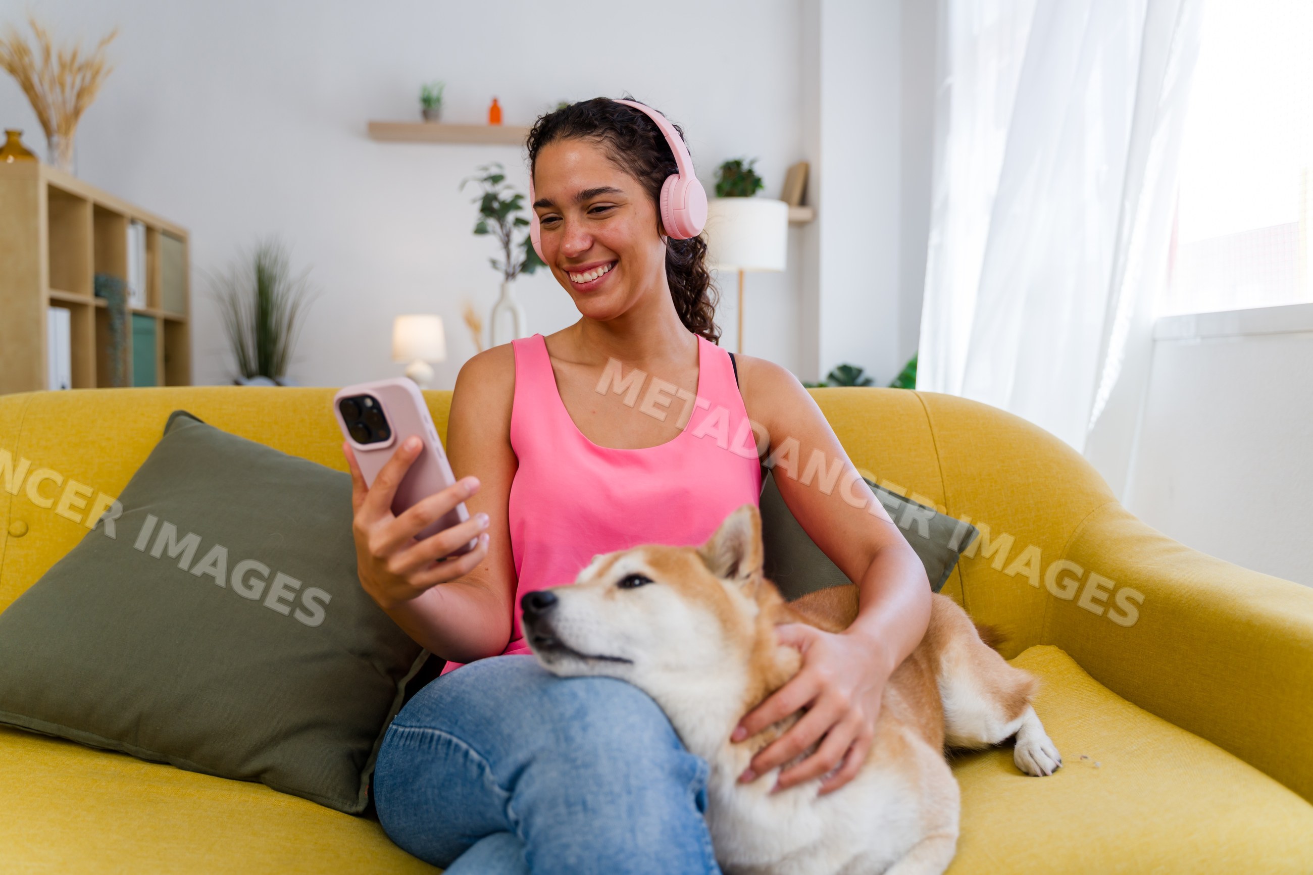 A Hispanic woman listens to music and pets her dog on a yellow couch