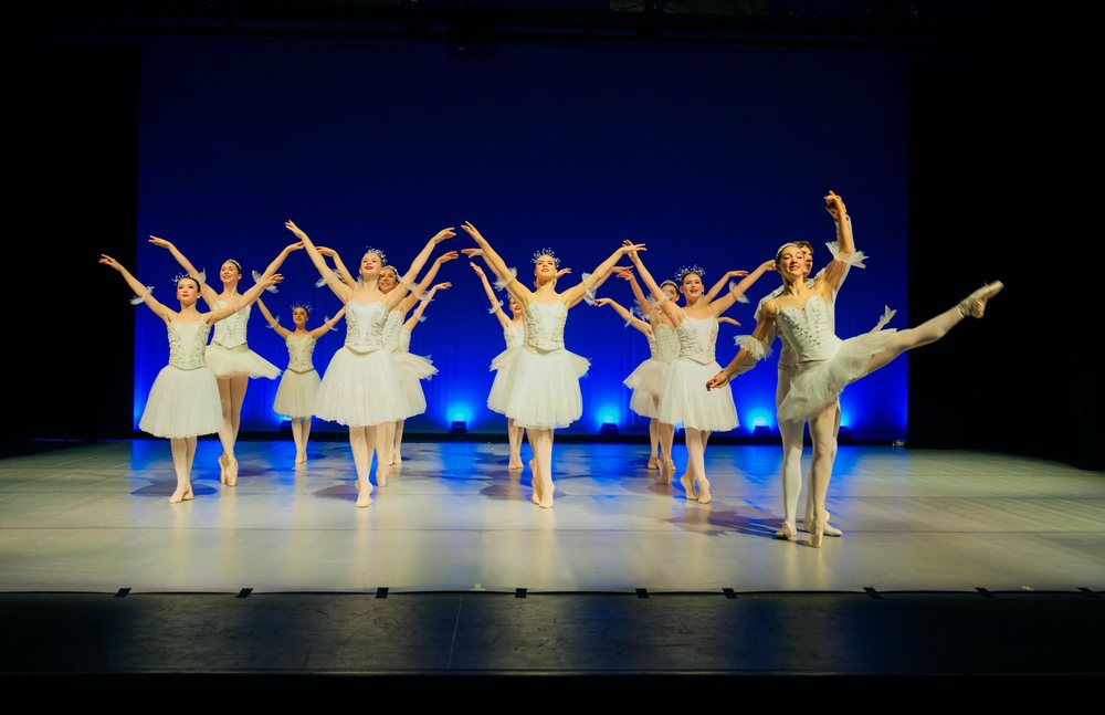 Ballet dancers perform holiday-themed dance on stage in white tutus