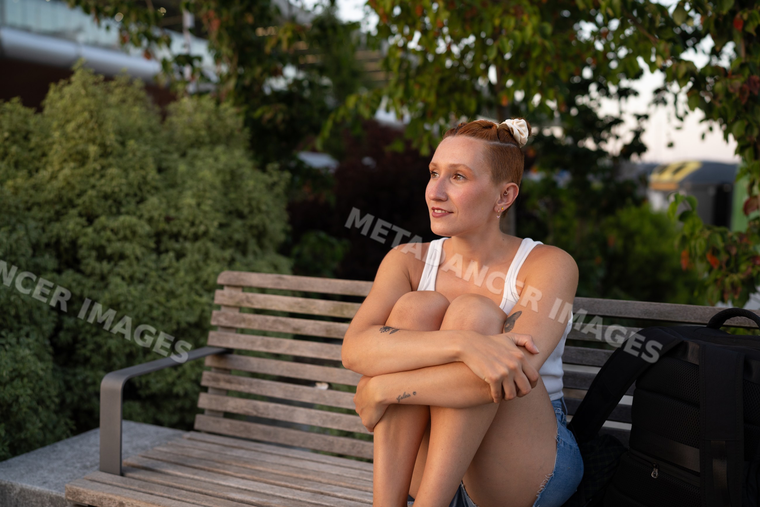 A white woman sits relaxed on a wooden bench in an urban park