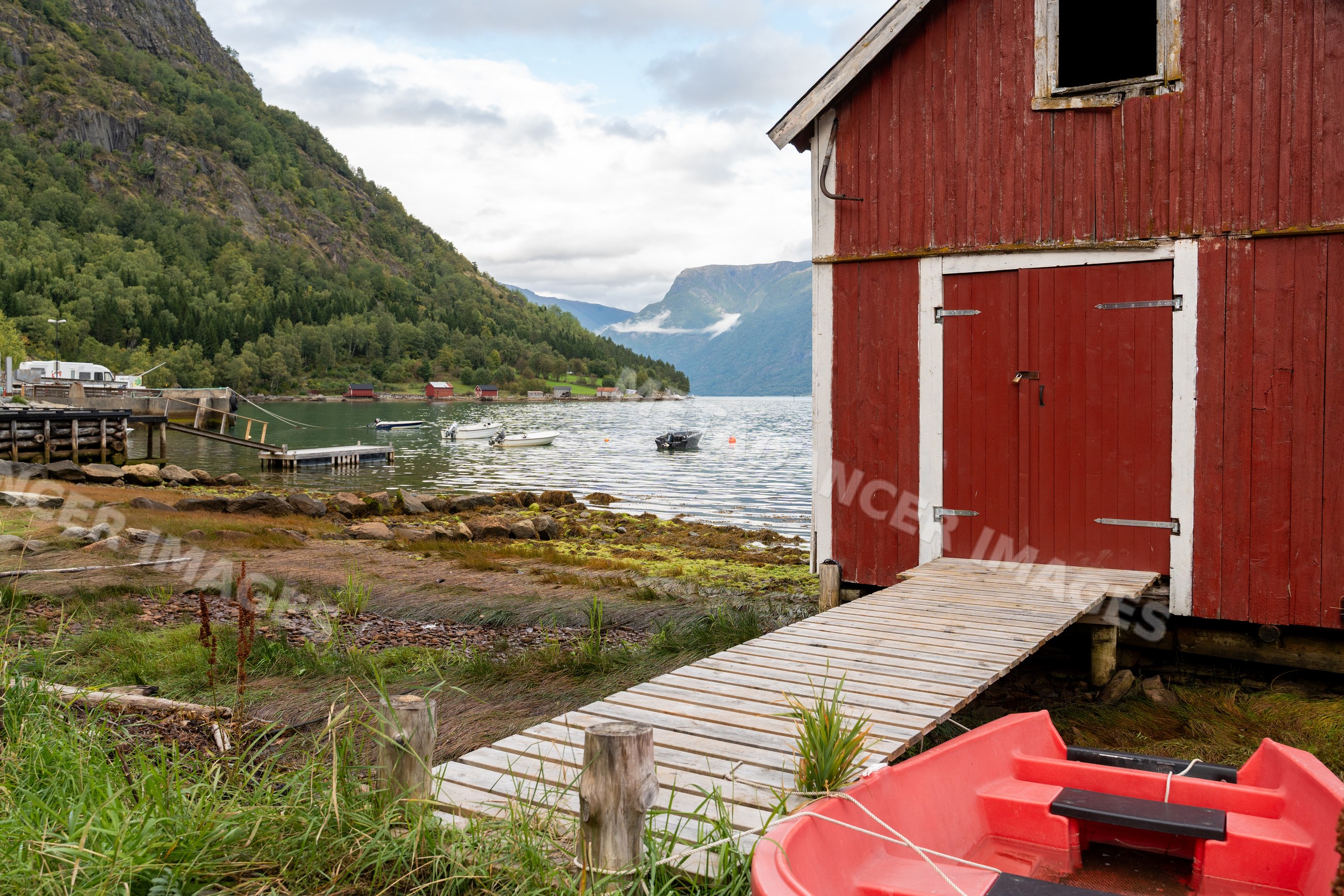 Red boathouse and dock with rowboat at norwegian Fjord waterfront