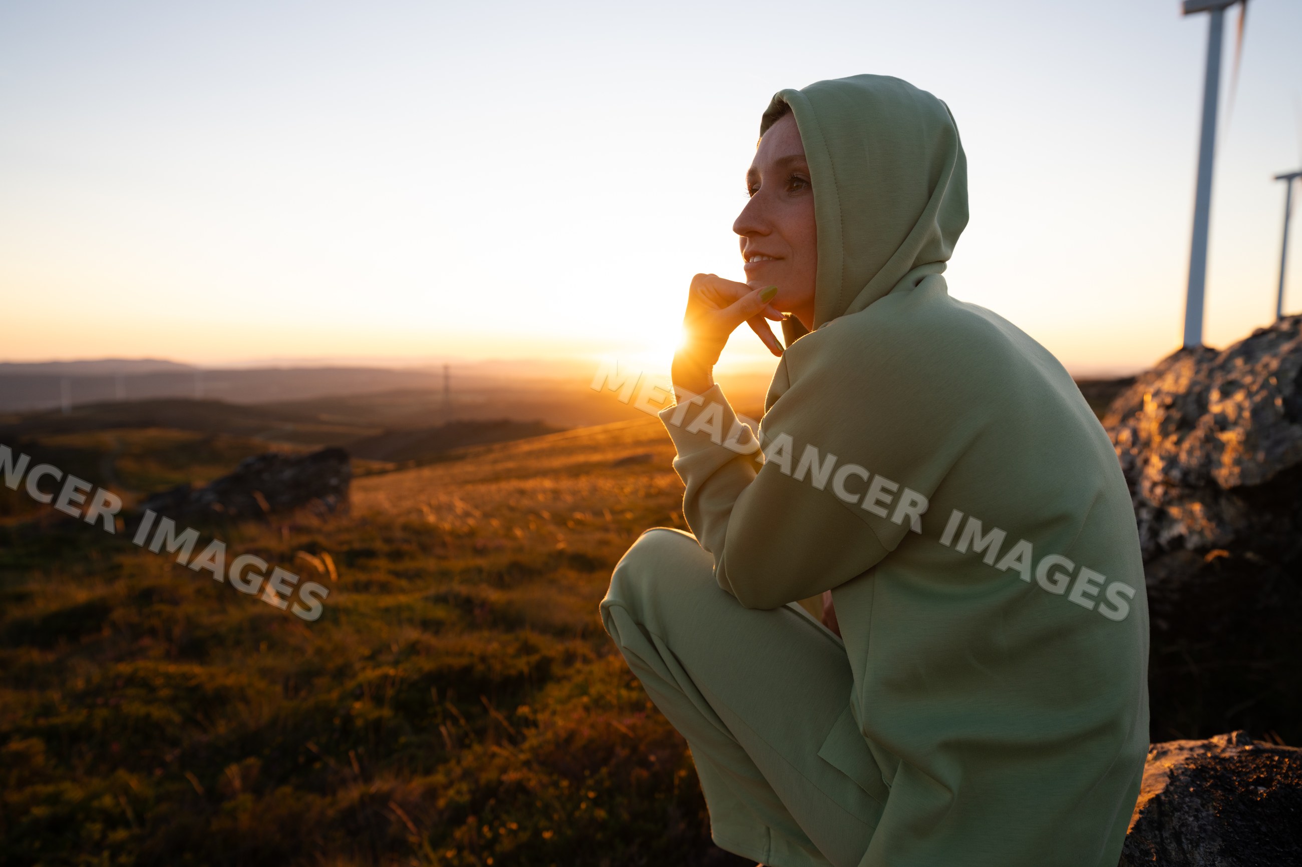 White Woman wearing hoodie sitting outdoors at sunset in Galicia Spain