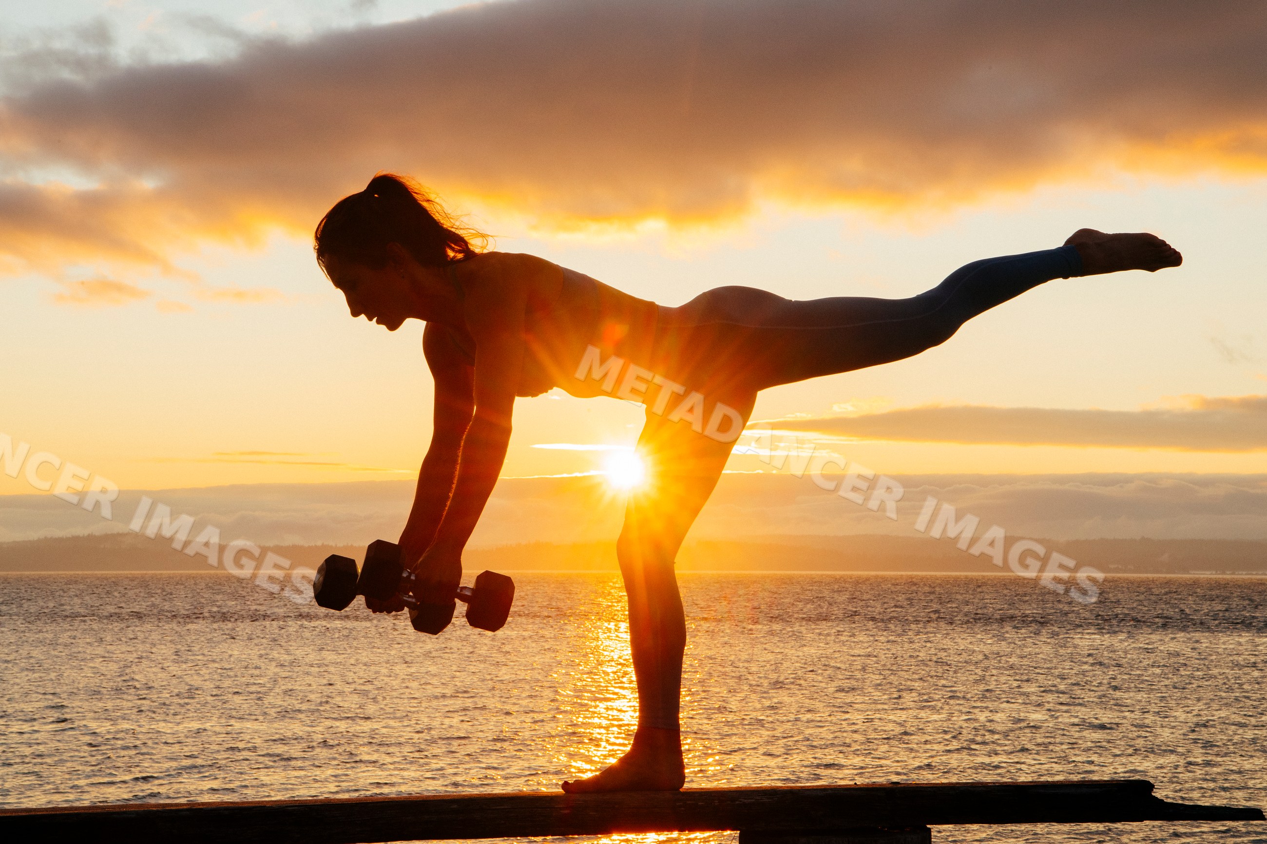 White woman holding dumbbells balancing on one leg