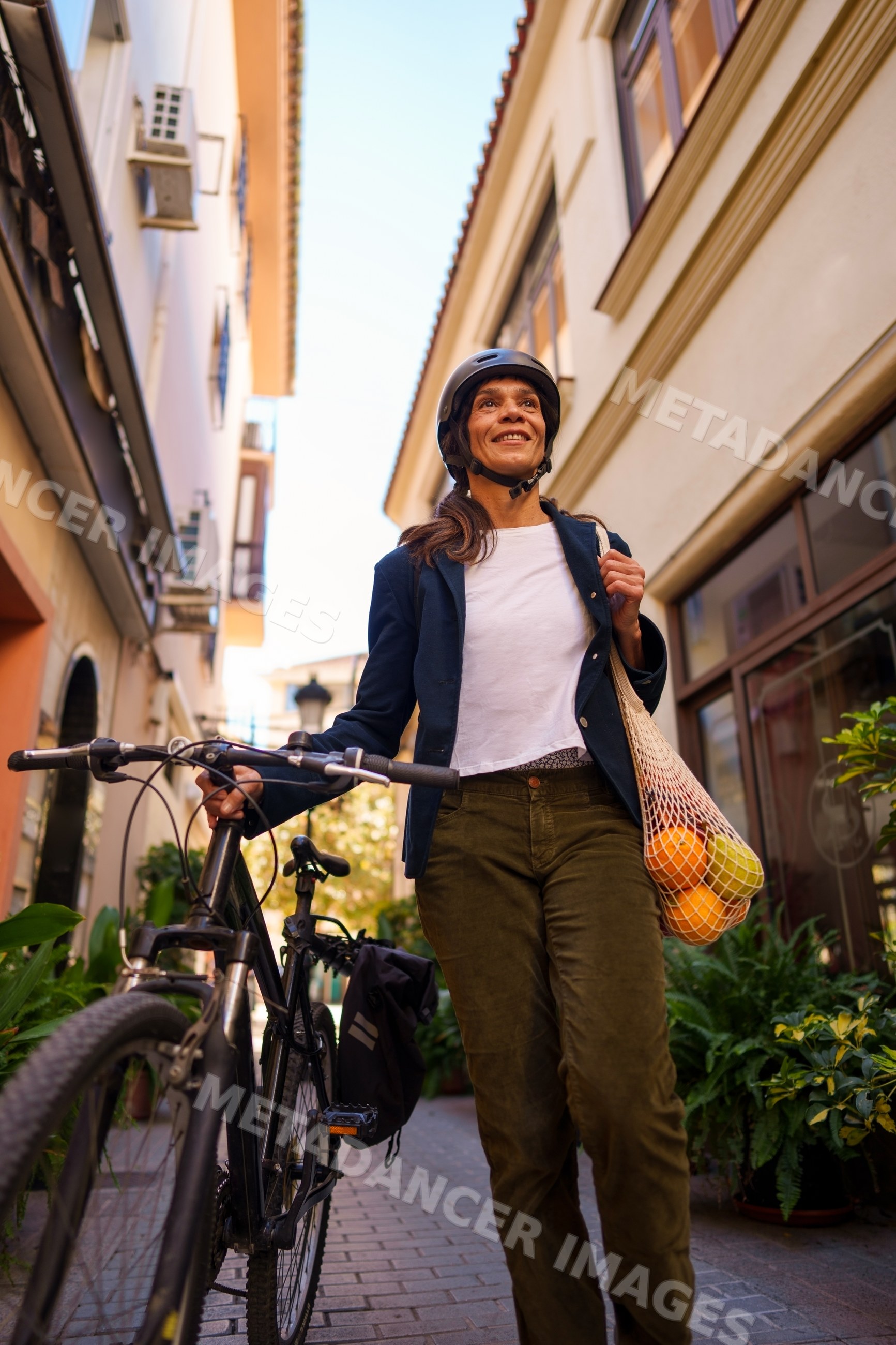 Hispanic woman walking bicycle with fruit bag on street in a street