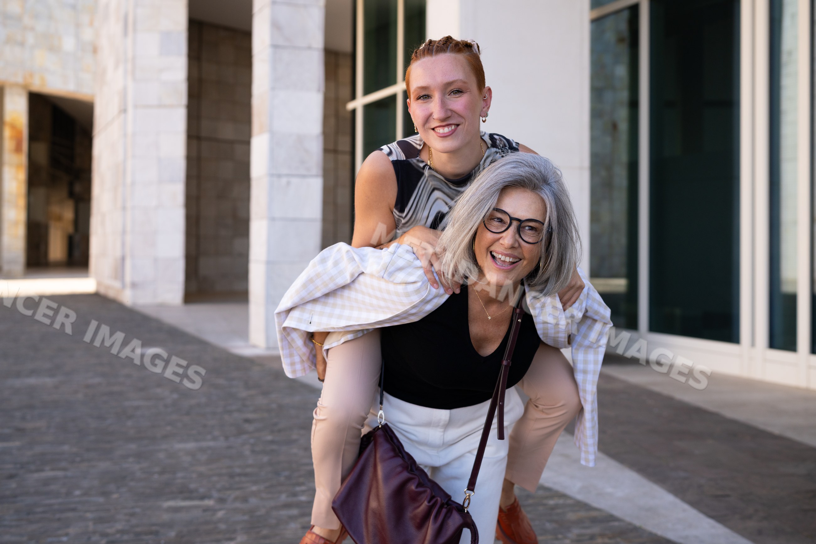 Two white women sharing a piggyback ride outdoors in an urban setting
