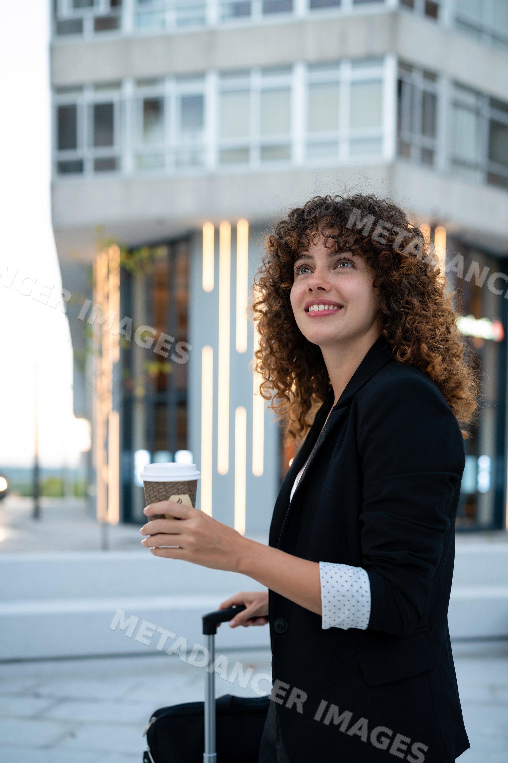 Young business white woman holding coffee and pulling suitcase
