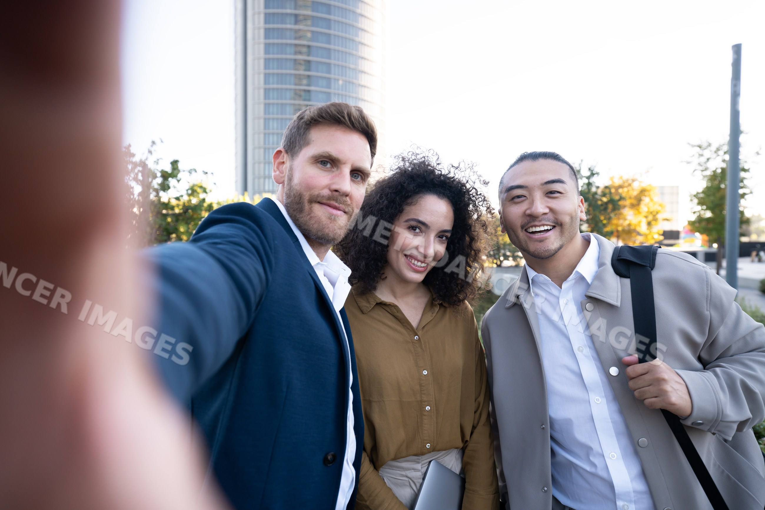 Three white people smiling and taking selfie outdoors
