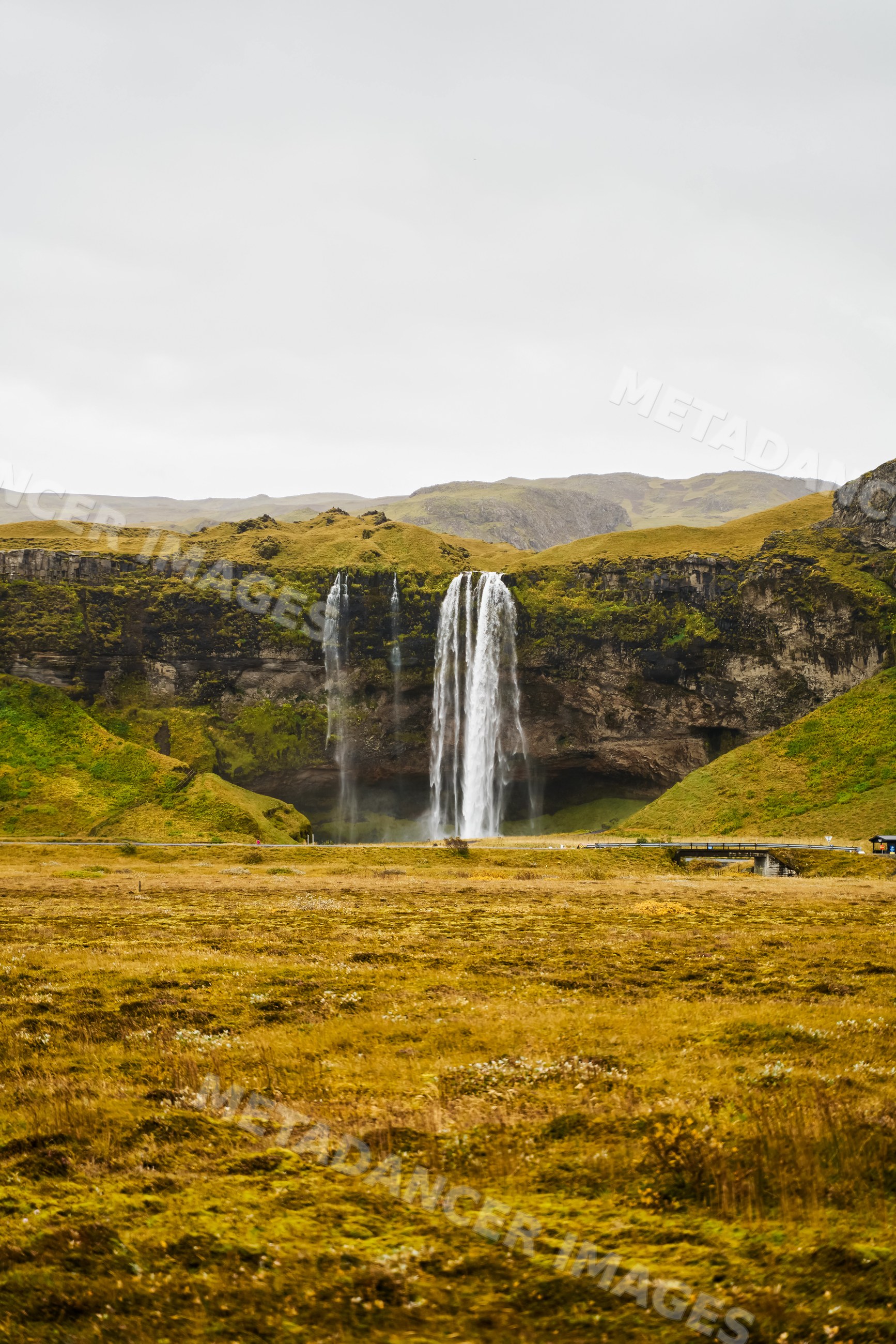 A wide waterfall cascades down rocky cliffs in a grassy valley