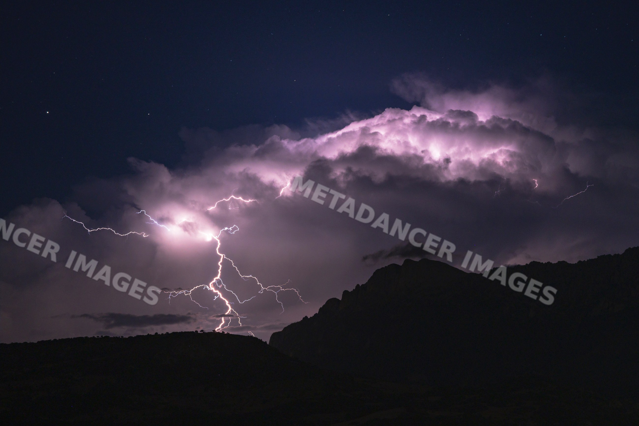 Lightning strike illuminating storm clouds over mountain