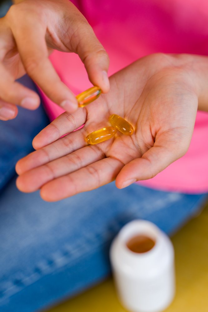 Hispanic Person holding yellow softgel pills with pill bottle
