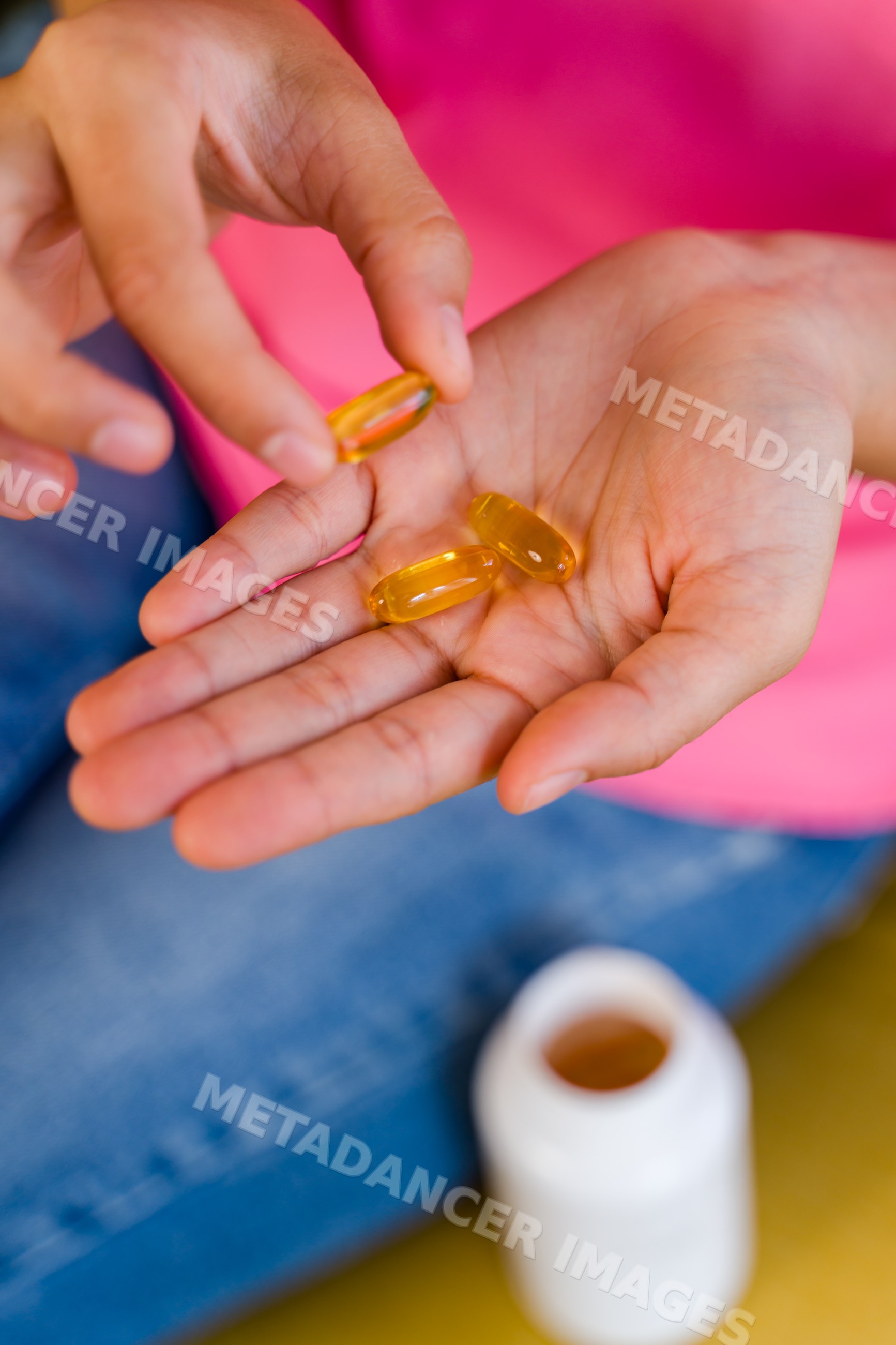 Hispanic Person holding yellow softgel pills with pill bottle